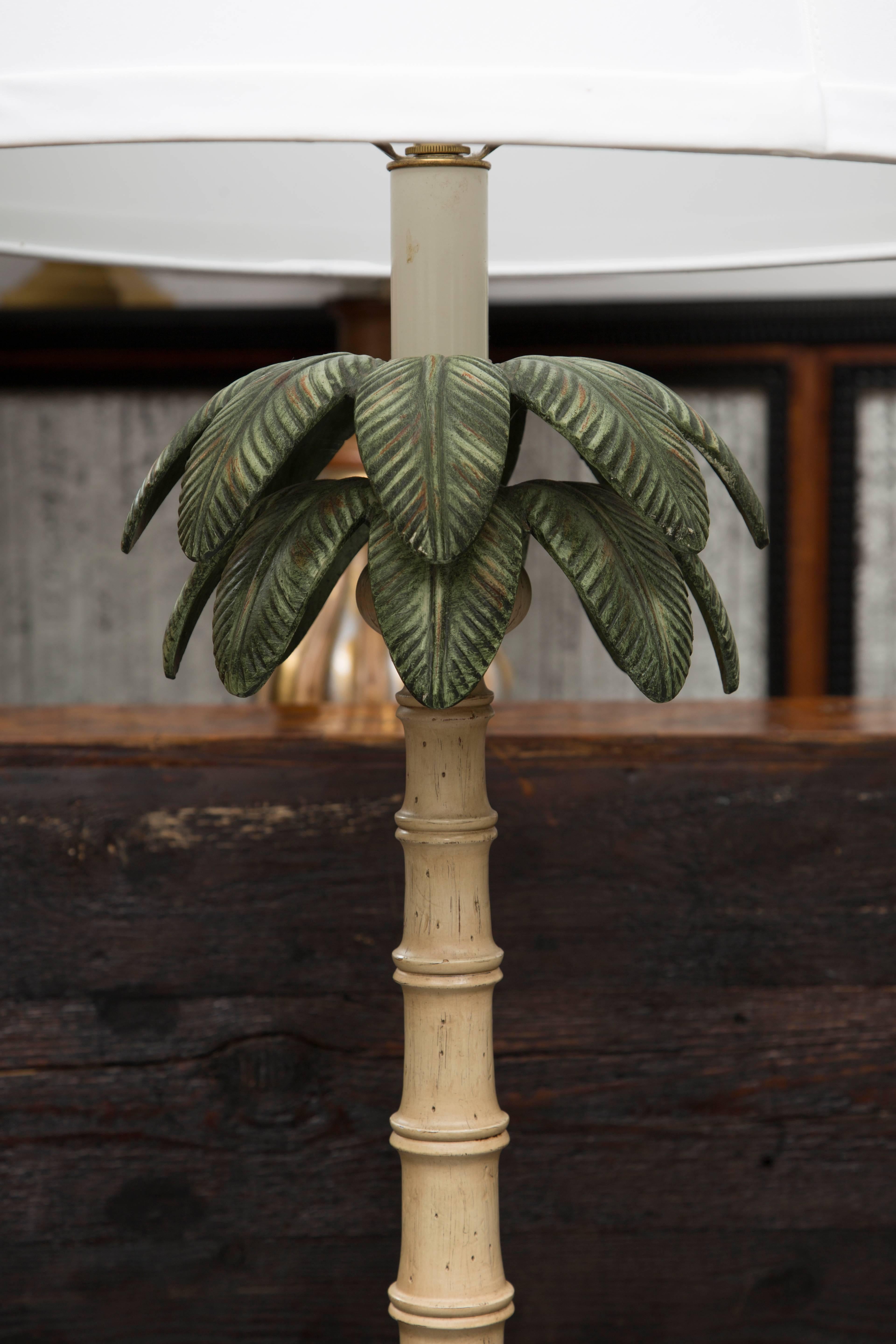 This polychromed tole floor lamp is in the form of a palm tree with green fronds above a cream shaft situated on a square base, 20th century.