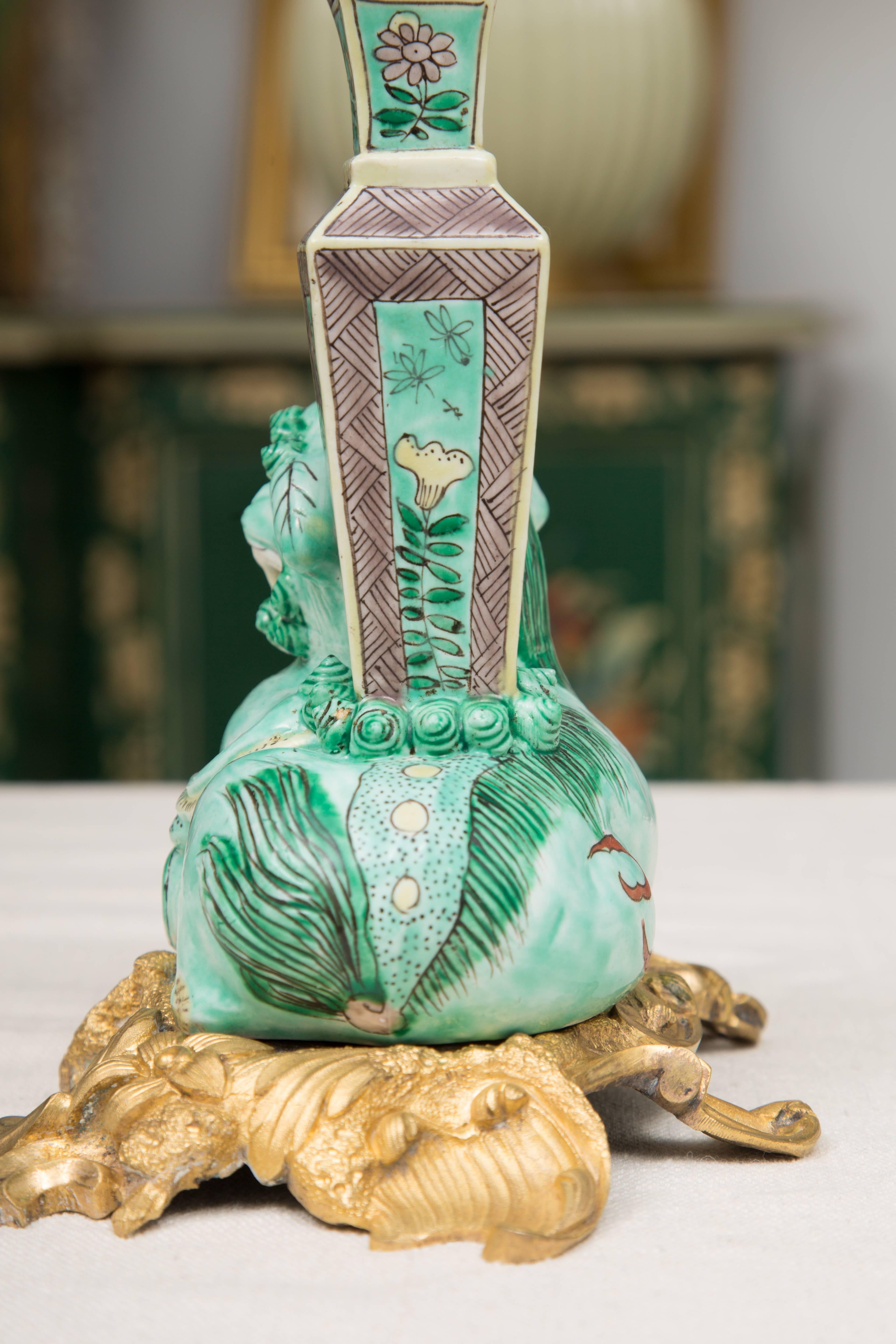 This is an elegant pair of beautifully hand-painted Chinese lions complemented by a bud vase, both situated on a scrolling bronze doré base, 19th century. Made for the French market.