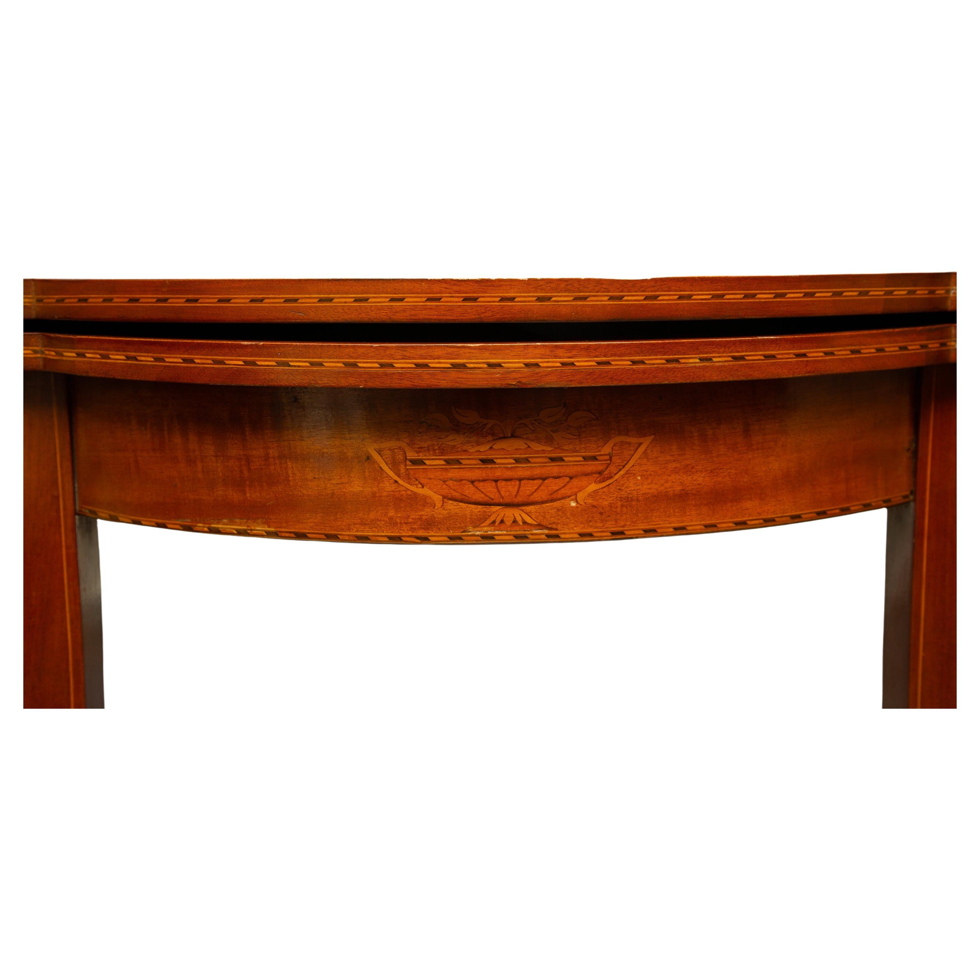 Se trata de una mesa de juego de madera de cerezo. 
La parte superior tiene una incrustación de madera satinada sobre un friso con incrustaciones y se eleva sobre patas rectas cónicas, finales del siglo XIX.