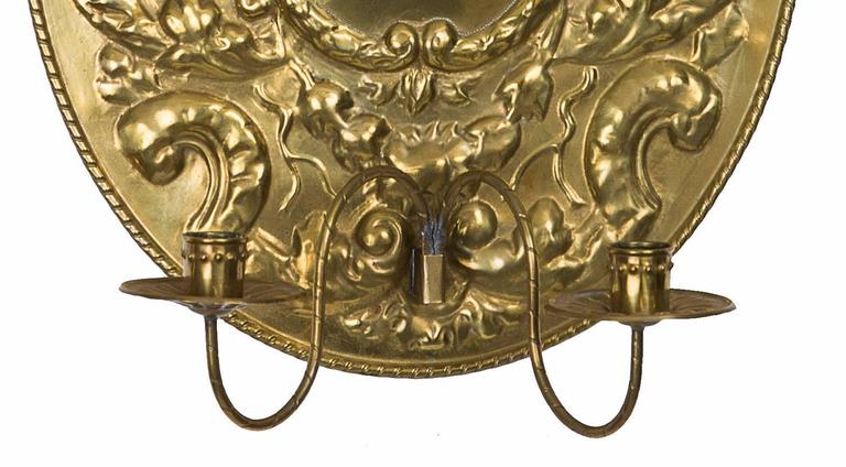 This pair of brass Dutch Baroque style sconces are oval in shape with heavy elegant repousse on the front under a forward projecting stylized crown and terminating in a pair of extended simple candle arms, late 19th century.