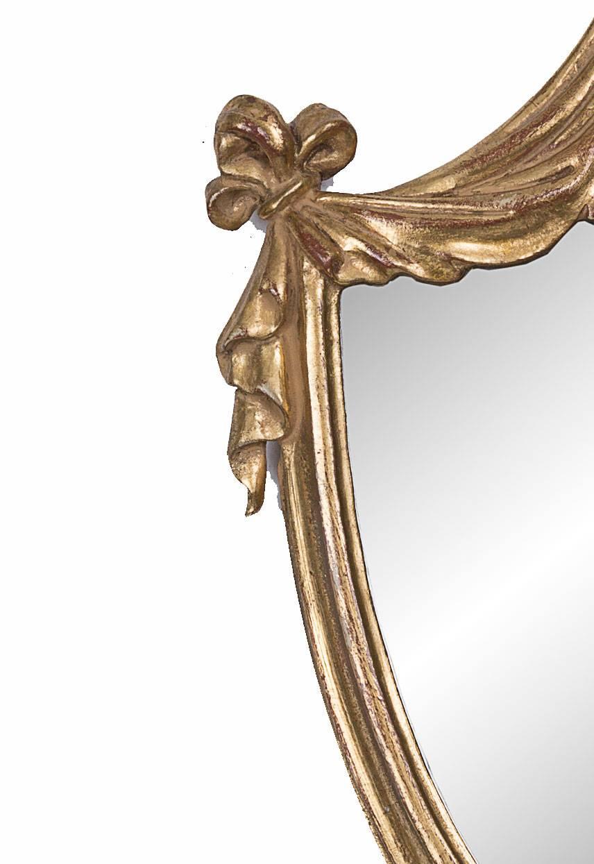 Questa elegante e delicata coppia di appliques a specchio in legno dorato inglese in stile Adams ha la forma di scudi armoriali con drappeggi sospesi da un importante arco centrale con due bracci a candela che emanano da un medaglione nella parte
