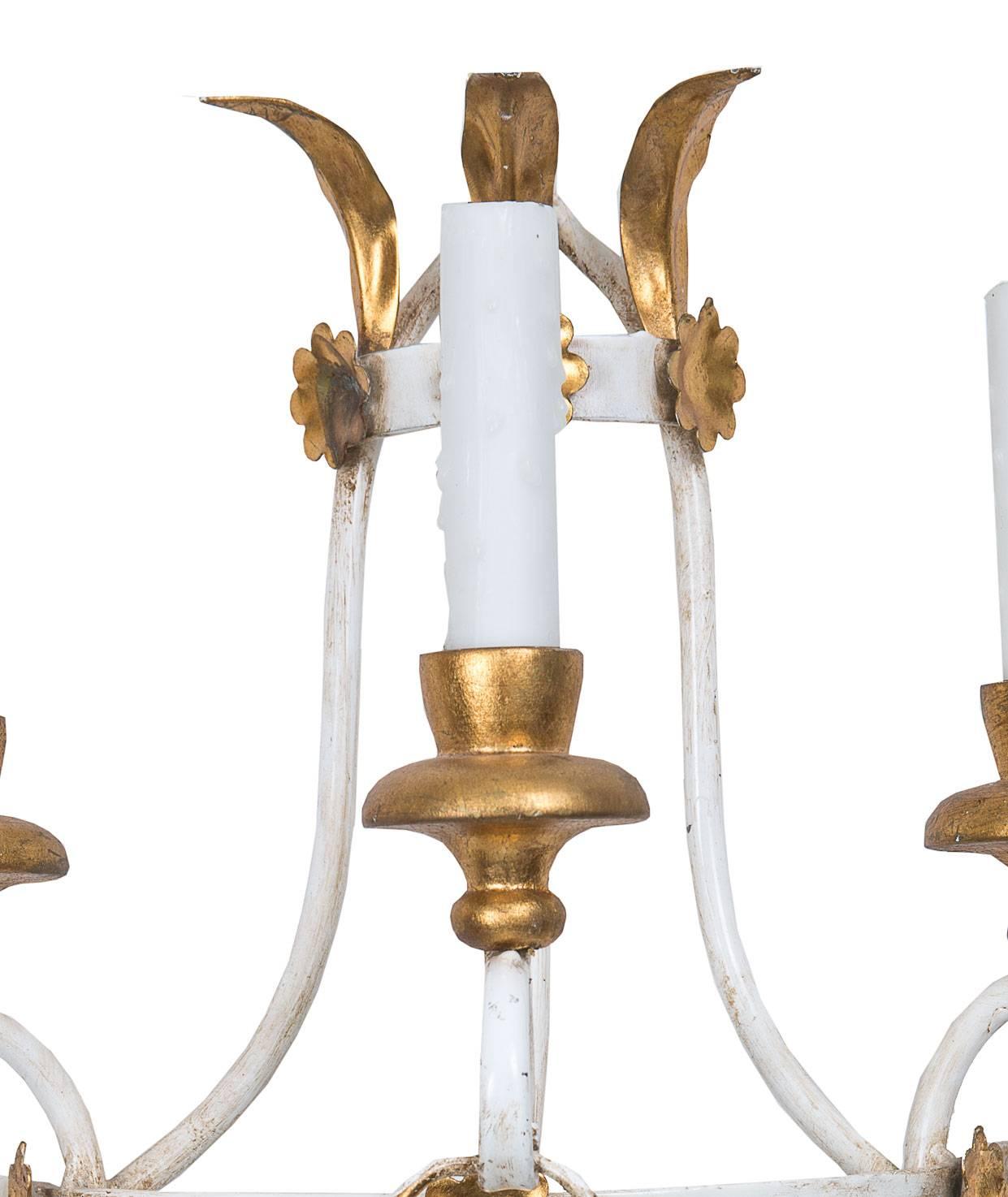 This lovely and delicate pair of Swedish white painted and parcel-gilt electrified sconces have a lantern form with three candle arms joined by a gilt metal juniper swag, circa 1950.