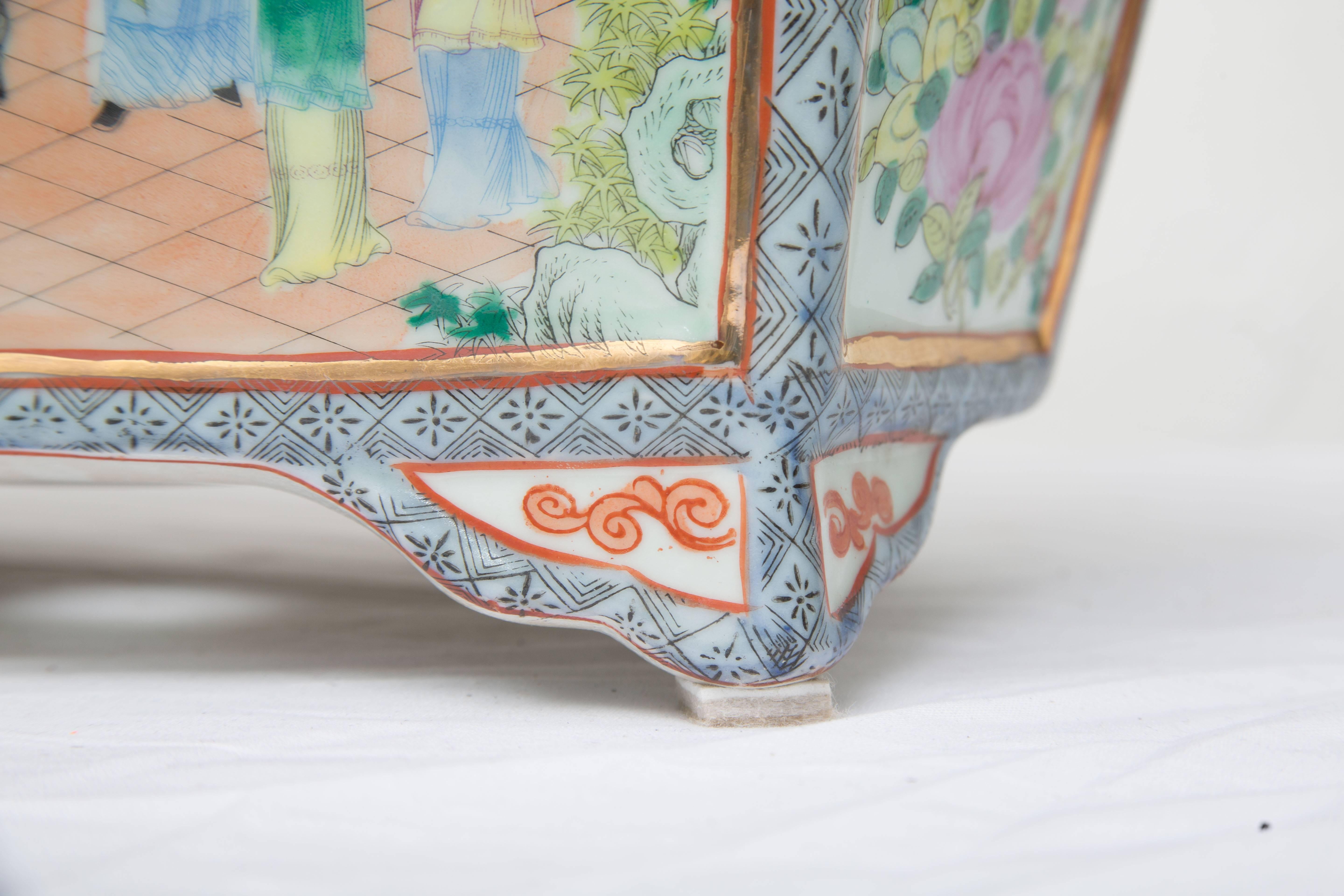 This stunning rose medallion rectangular ceramic jardiniere offers a sophisticated accessory for any fine interior. The piece is hand-painted with courtyard scenes and panels of lotus blossoms, and a pattern of fruit. Drainage holes in the base