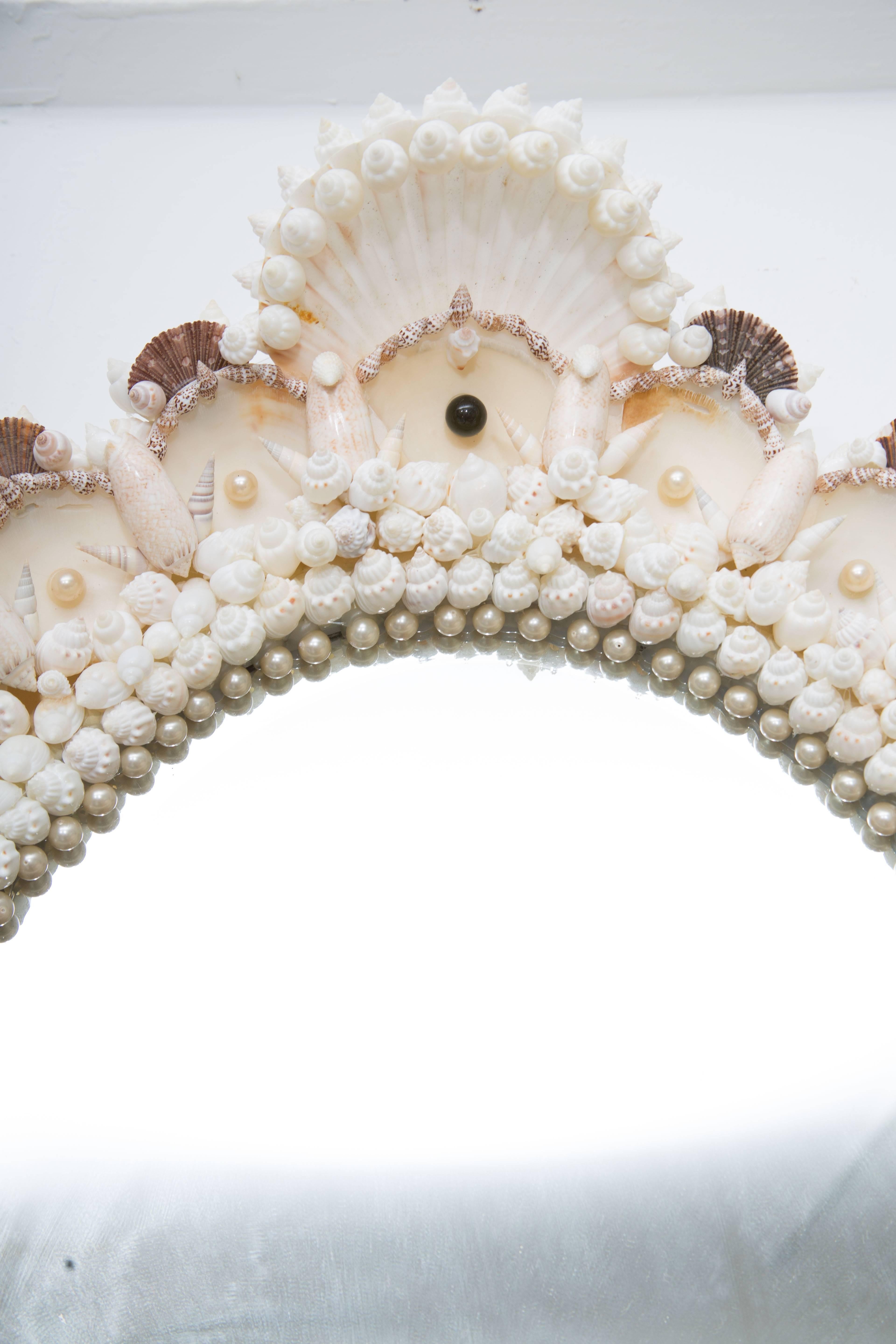 This romantic and delicate custom oval mirror has a beautiful frame of artistically encrusted shells accented with simulated pearls, circa 20th century.