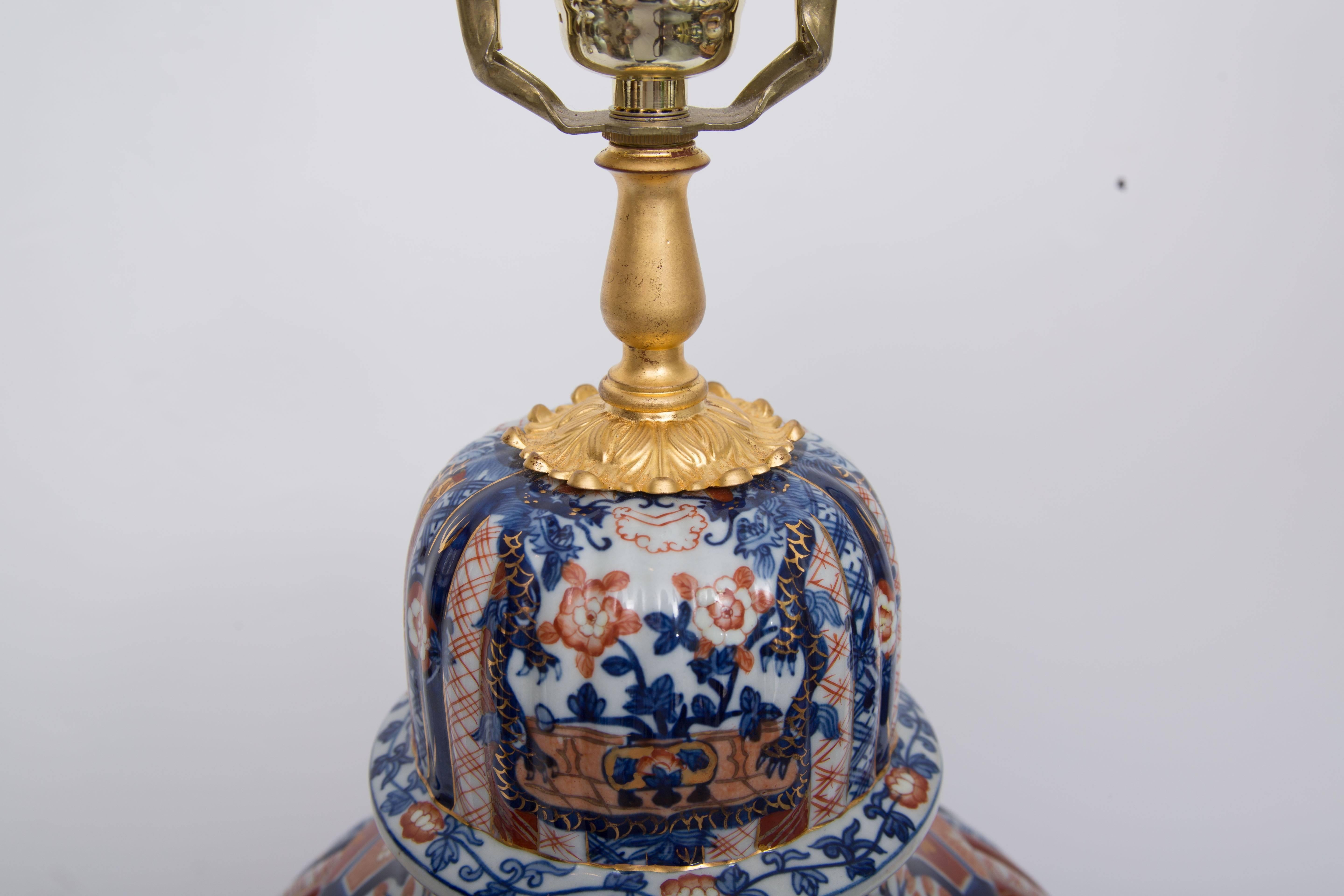 This elegant Imari style vase with ribbed design has been converted to a lamp situated on a carved giltwood base with lotus design and giltwood cap, circa 20th century.