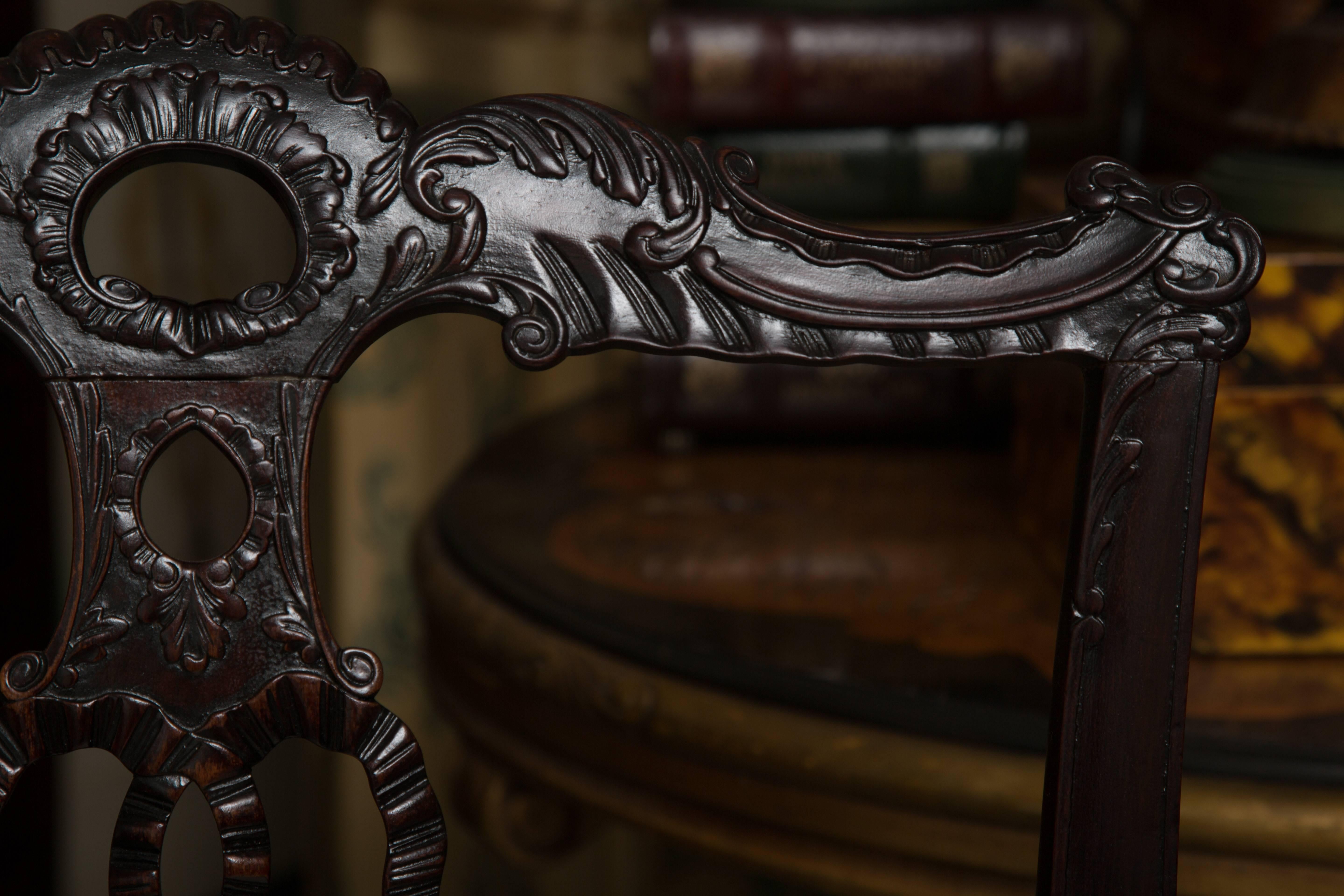This lovely pair of dark mahogany English armchairs have delicately carved backs plats in the form of flowing ribbons tied in a bow under a pierced top rail above a padded seat over narrow carved apron. The chairs are supported by cabriole legs,