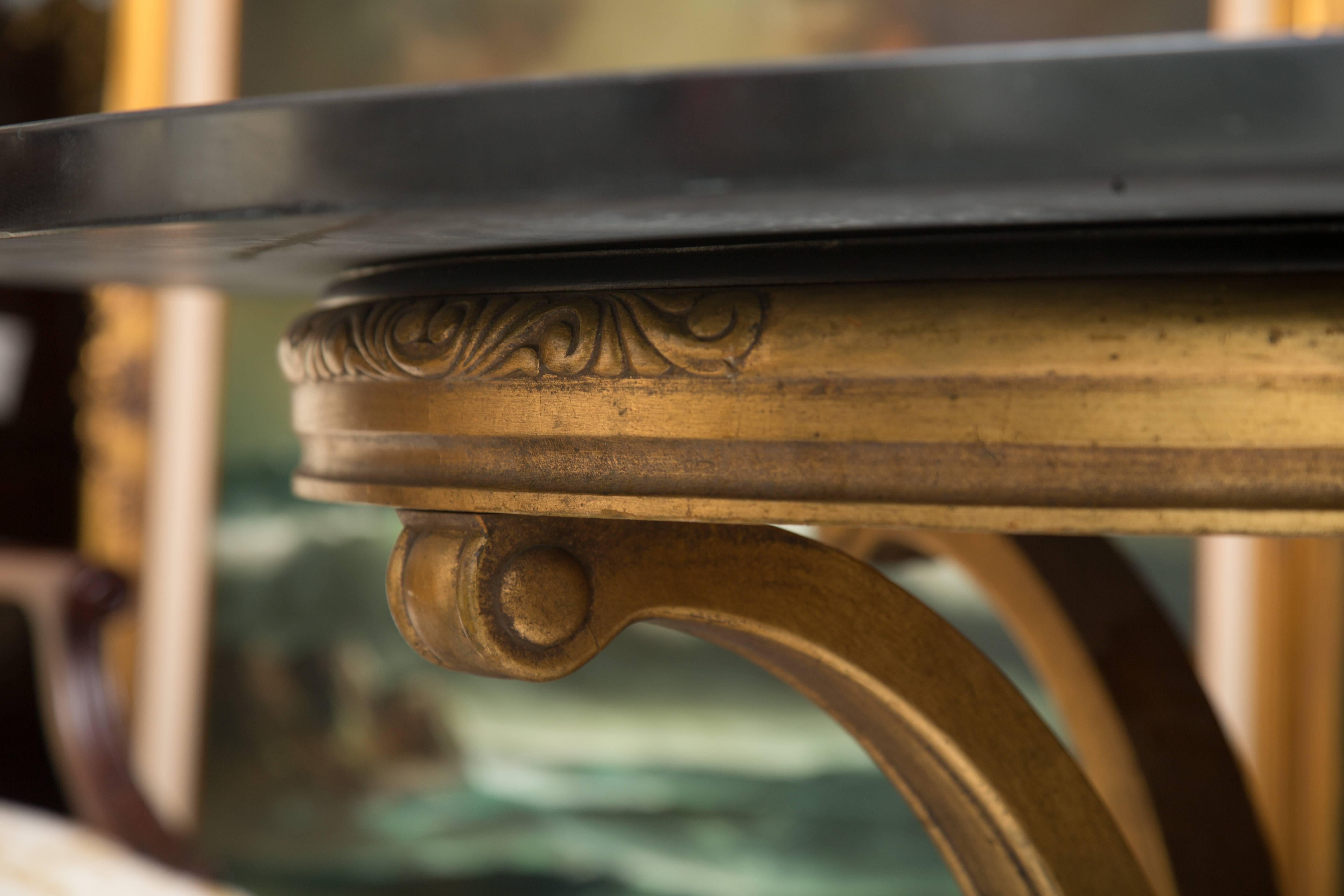 This interesting center table has a carved Italian giltwood base supporting a circular black granite top inlaid with two concentric white granite circles, 20th century.