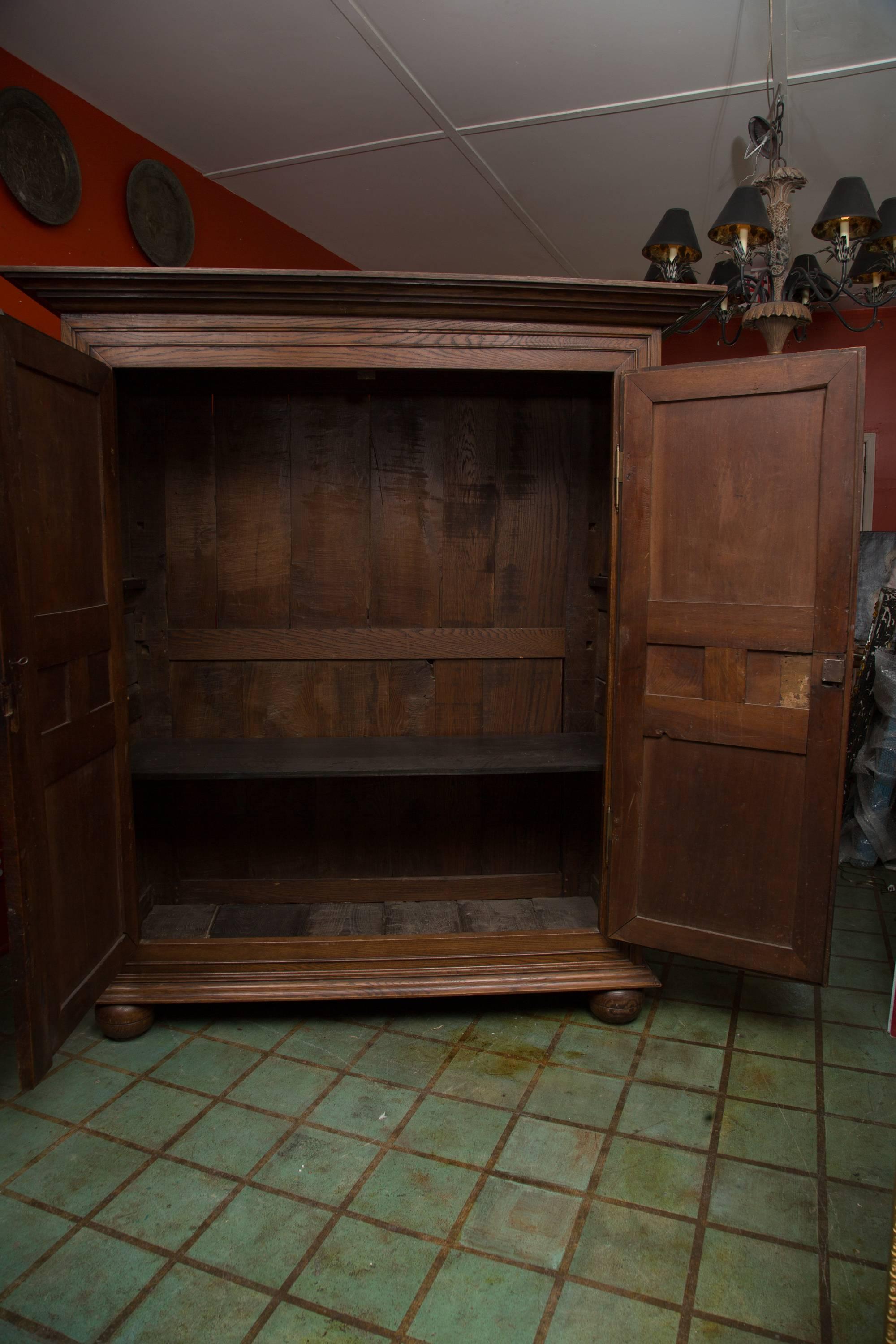 This French oak armoire has a shaped cornice over two long paneled doors enriched with raised geometric panels above a shaped apron and raised on bun feet, 18th century with restorations.
