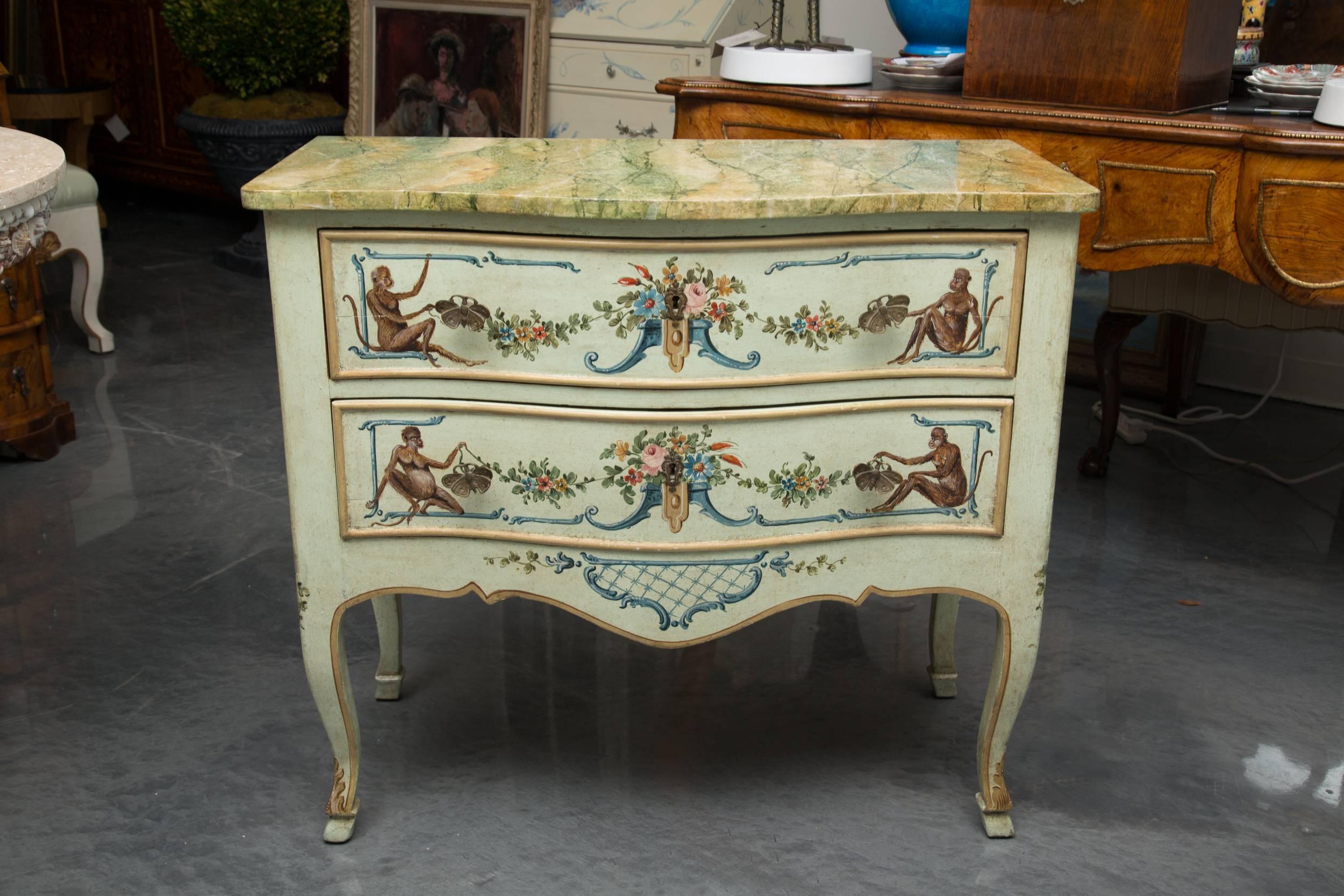 This is a whimsical, yet sophisticated Venetian commode artfully  painted with monkeys flanking floral bouquets and swags on a soft blue background. A beautiful highly glazed  faux marble top offers a realistic image of polished marble over two long