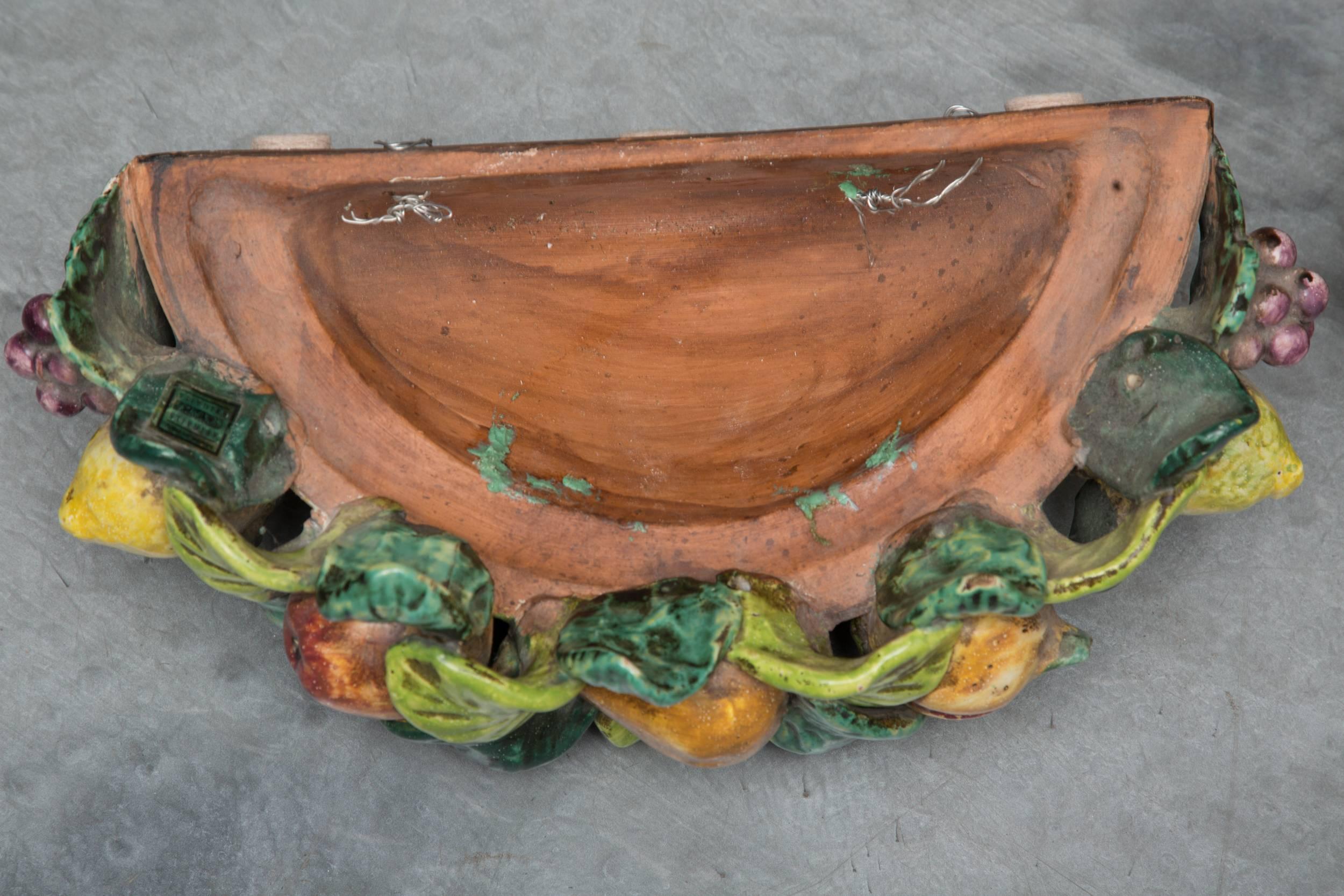 This pair of Italian terracotta wall pockets is crowned by a garland of painted and glazed leaves interspersed with fruits of pomegranates, lemons and pears, creating the feel of a Tuscan terrazza, 20th century.