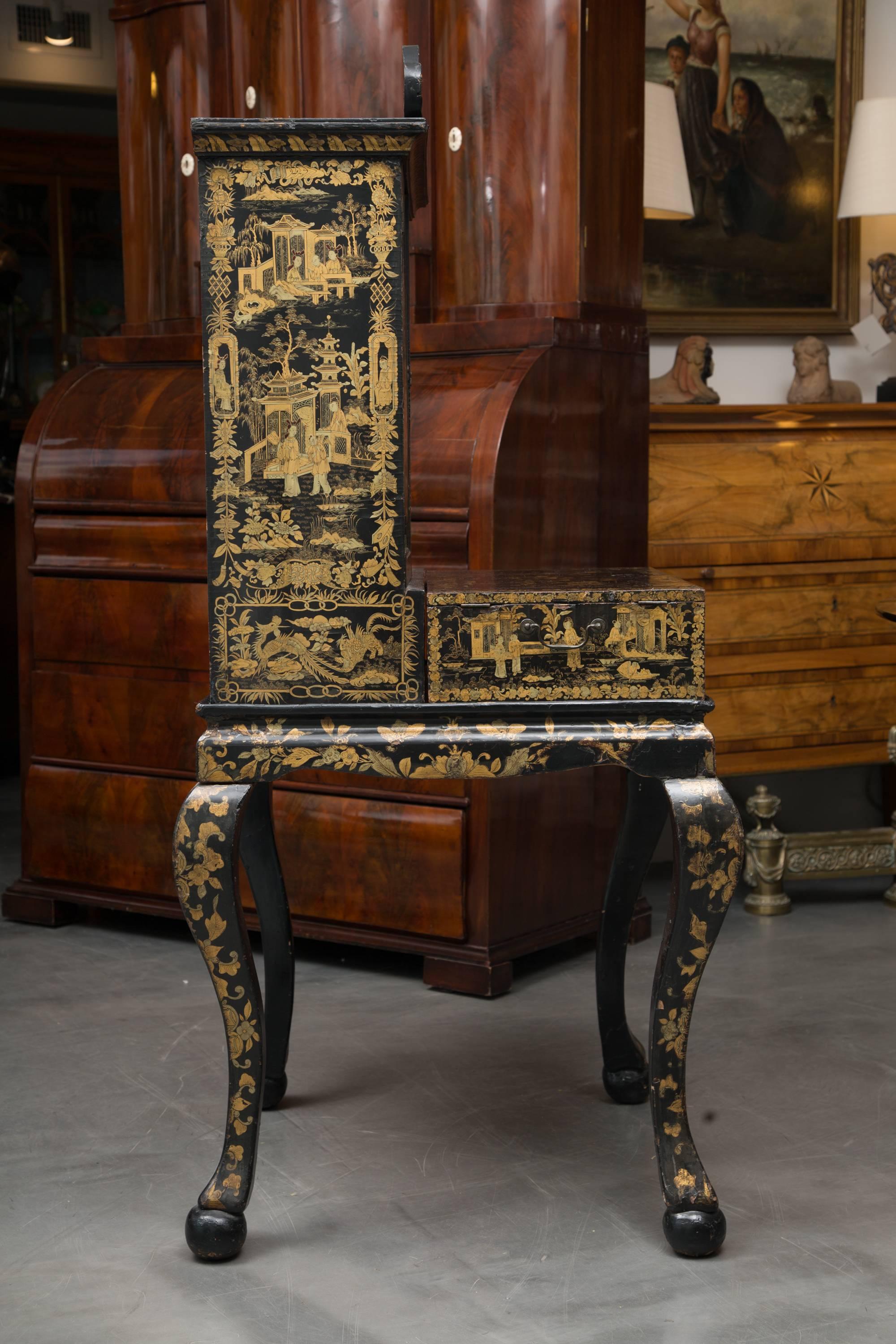 This is an elegant English black lacquered English Queen Anne cabinet chest on Stand decorated overall with gilt chinoiseries. This case piece was originally a traveling secretary.  The top section has a cornice with a broken pediment over a