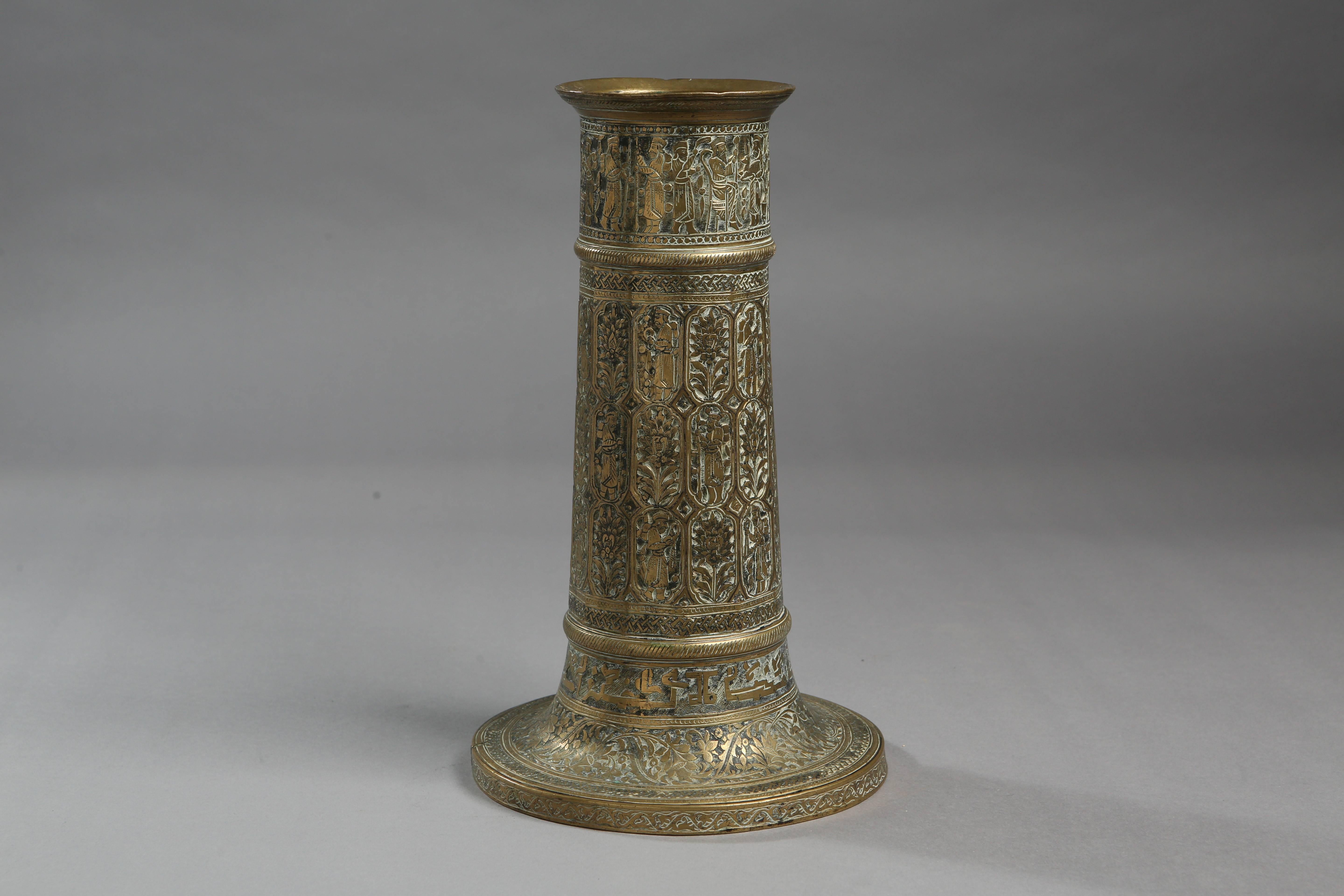 This 19th century brass Qajar candlestick features figural and vegetative imagery along with floral and leaf motifs and an inscription round the bottom.

Measurements: 29cm tall x 15.5 cm base diameter.