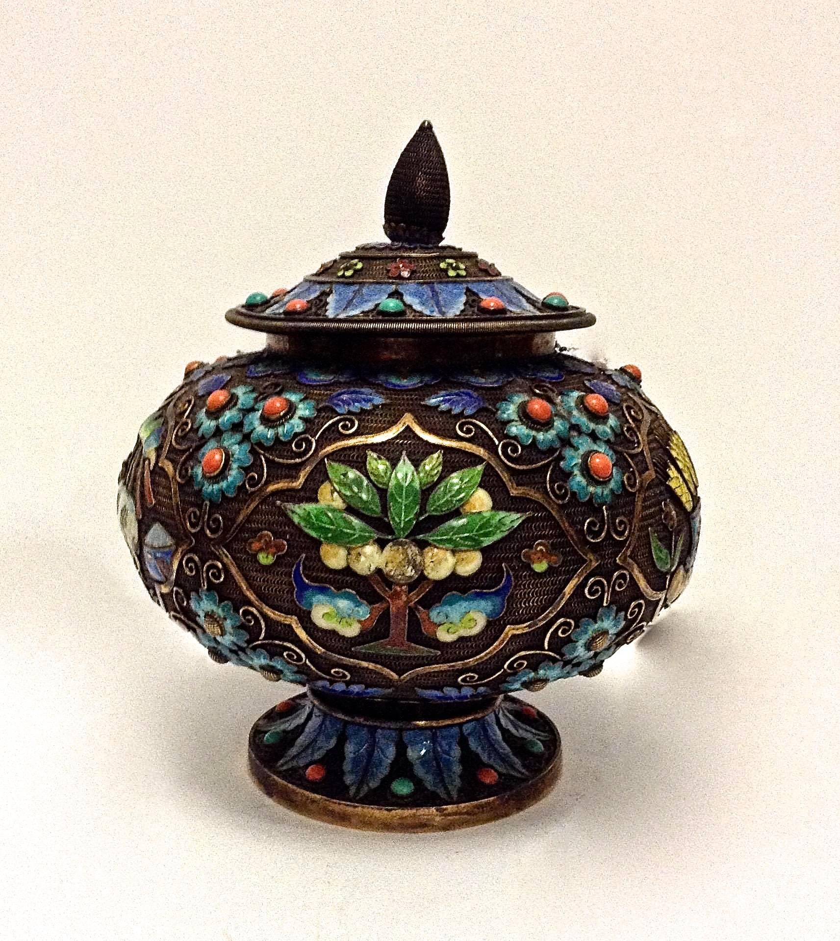 A Chinese export gilt-silver and enamel box with a blue floral and leaf radial design on the lid. It is of a bulbous shape that features four framed enamel 'scenes' within it, including: vegetables with wheat in a vase/shield with a red triple cross