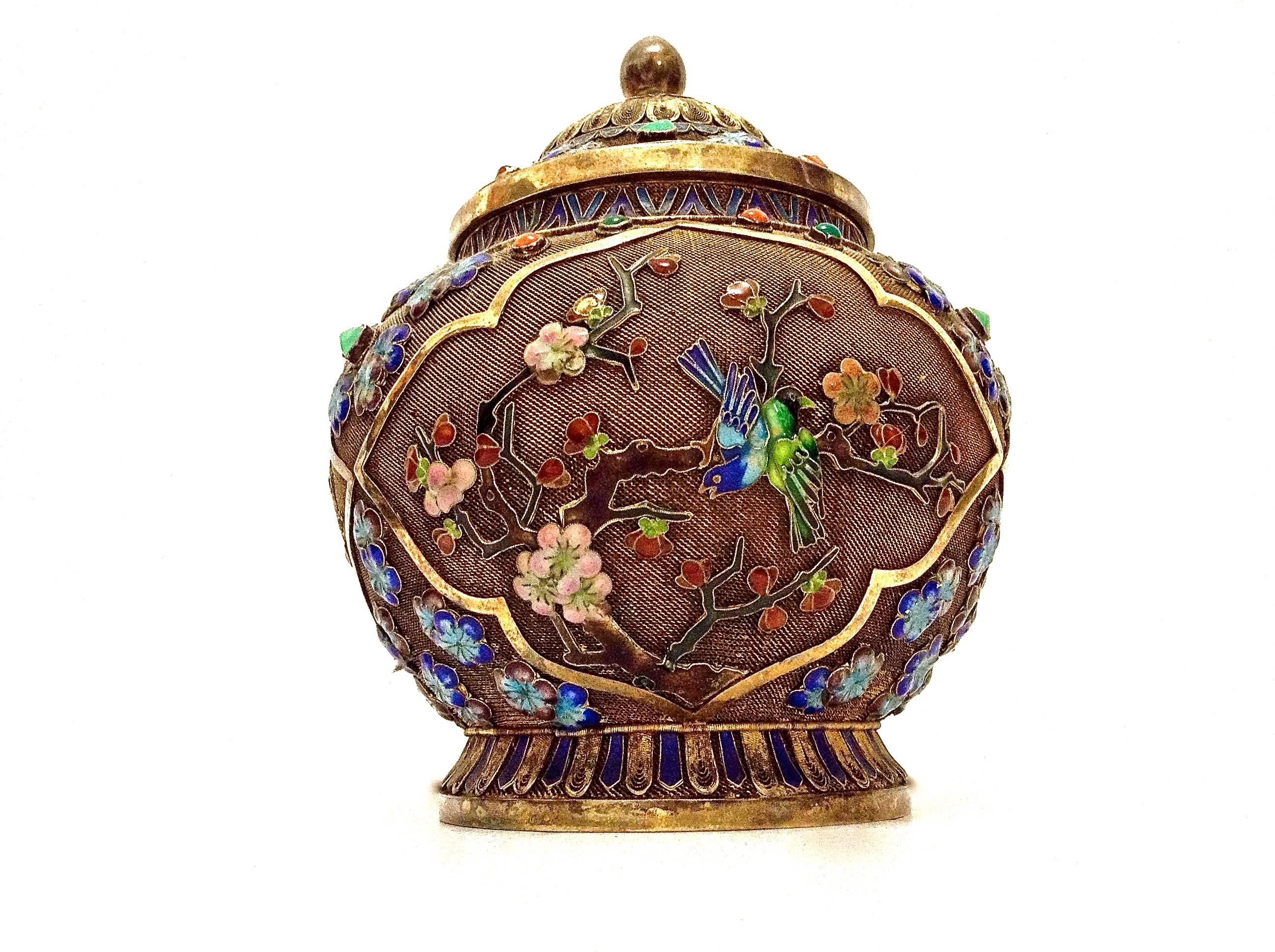 A late 19th century Chinese export silver-gilt and enamel box featuring flowers, birds and butterflies. The box has a blue heart shaped radial design on the lid next to the finial and filigree and mesh metalwork all-over. It is of a bulbous shape