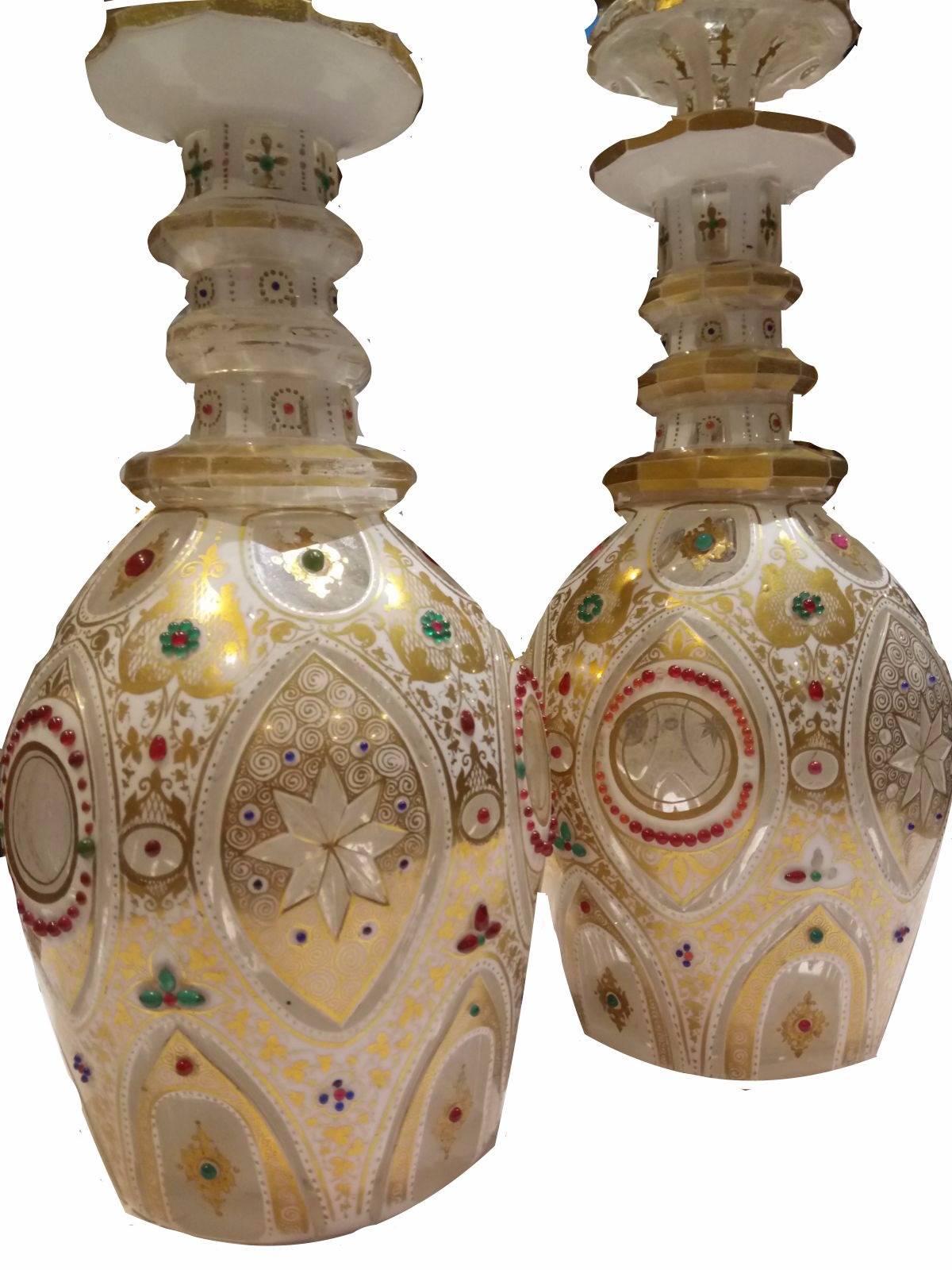 A near pair of Bohemian clear and white flash-cut and enamelled glass bottles with spire tops. They are painted with decorative gold designs and feature green and red 'jewels'.