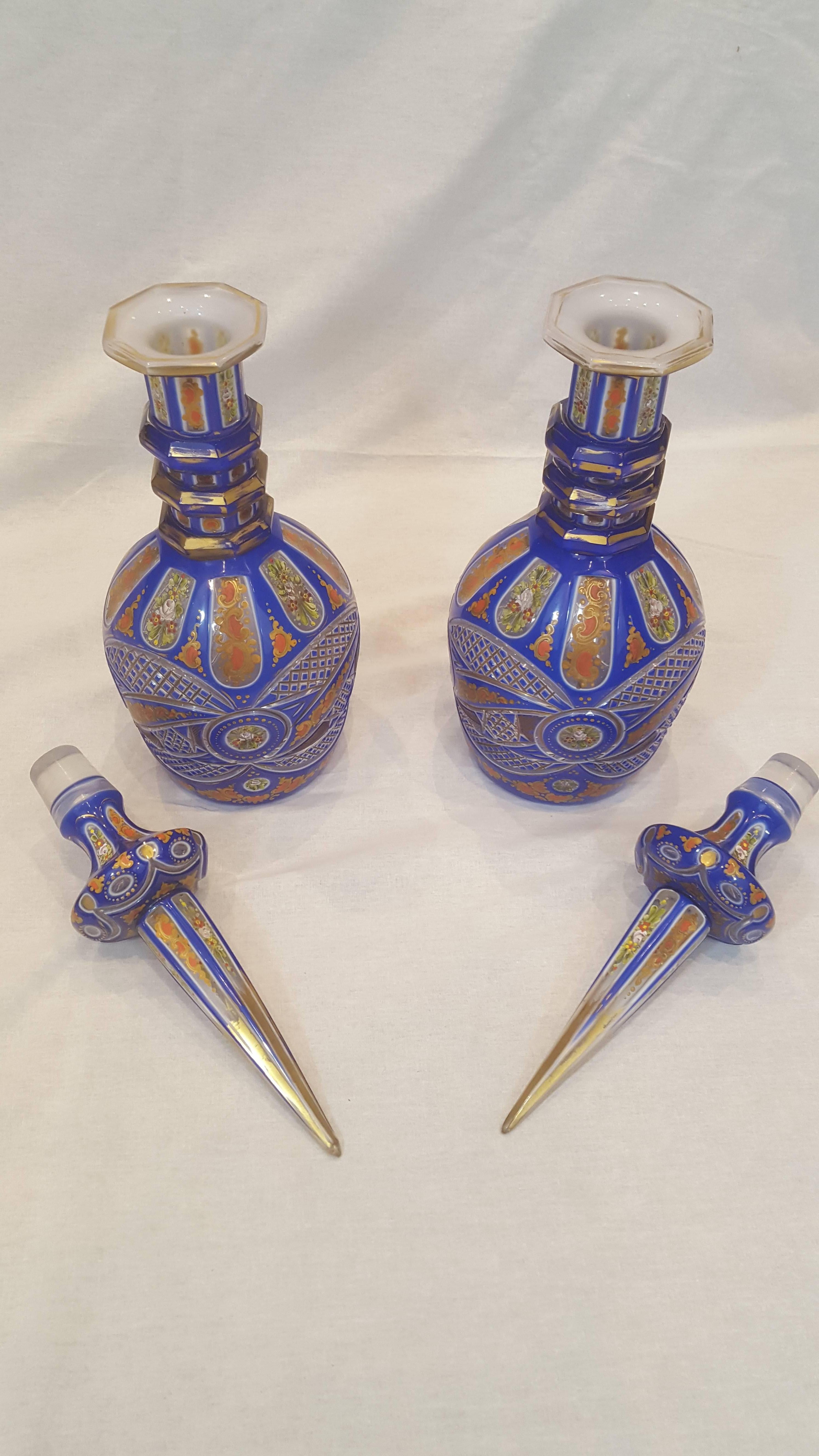 A pair of blue colour Bohemian cut and enamelled glass decanters with spire stoppers. They feature three rings around their necks, and are each decorated in a floral and foliate motif. Made for the Persian market.