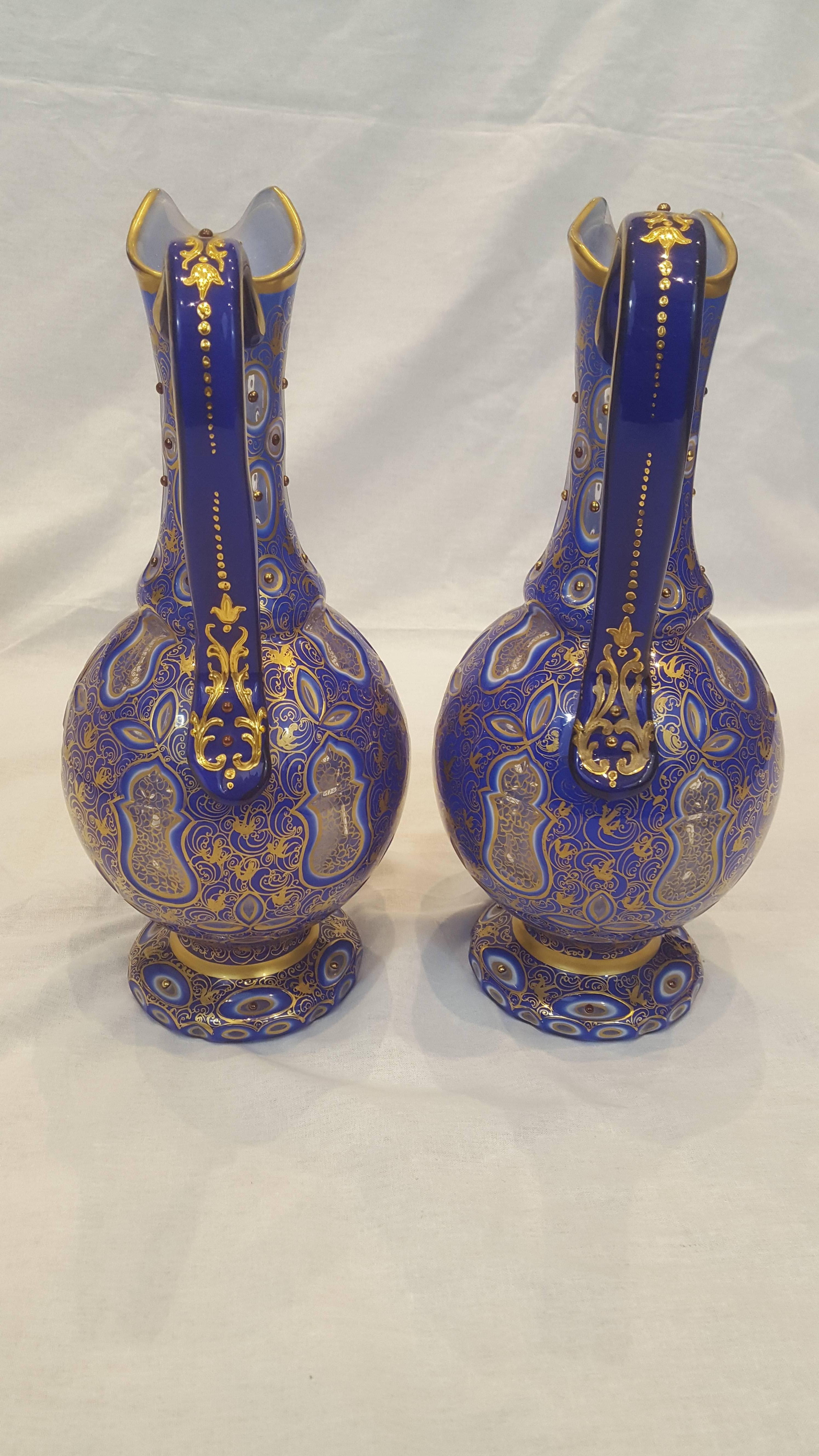 Made of a round bulbous body in blue glass with white overlay sitting upon a socle base, they feature a single handle. Each of the ewers are enamelled and gilt in a swirling decorative gilt motif with applied 'jewels'.
Made for the Persian market.