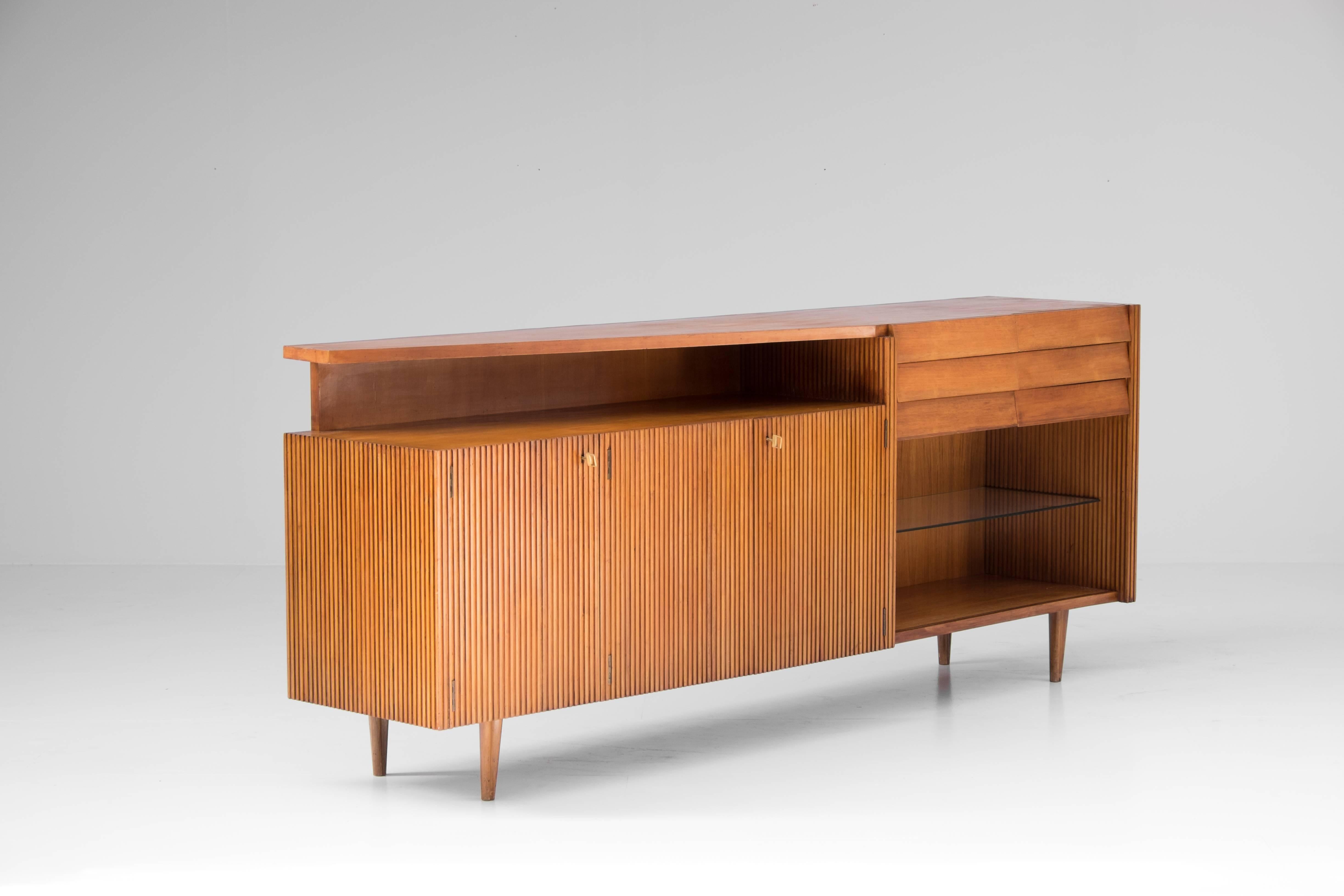 Italian sideboard produced during the fifties in pearwood. 

Large central storing space, sealable by three doors, flanked by an open display area with a glass shelf. Above, six drawers to the right.