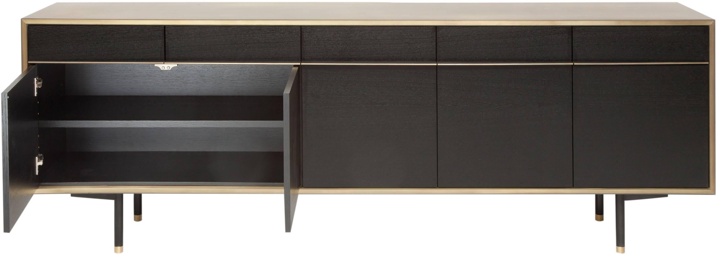 The glamorous and striking Tompkins sideboard has a brass encased in epoxy resin exterior with blackened white oak doors and interior and custom leather and brass pulls. The drawers are lined with brass and the cabinets have adjustable shelves. The