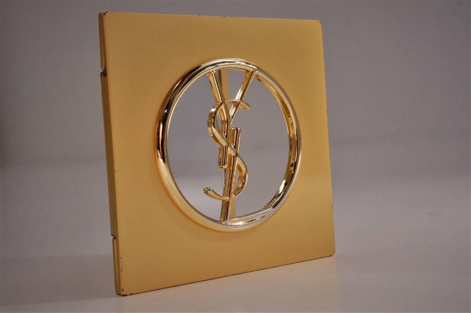 Yves Saint Laurent compact makeup mirror gold plated gilt with YSL logo and monogram velvet sleeve, circa 1980s, French.

At the focal point of this vintage compact mirror is the YSL logo. With the mirror below showing through the design is simple