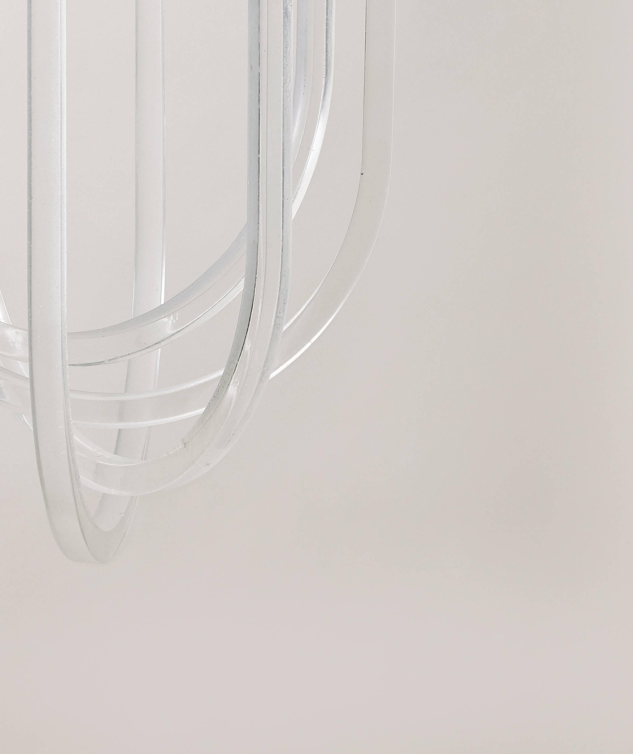Four cast-resin rings, equally-spaced around a brushed-brass light source, varied in length, with one looping under the next to create a spiraling illuminated choreography. The Cirrus Chandelier is suspended by a vertical brass rod with a