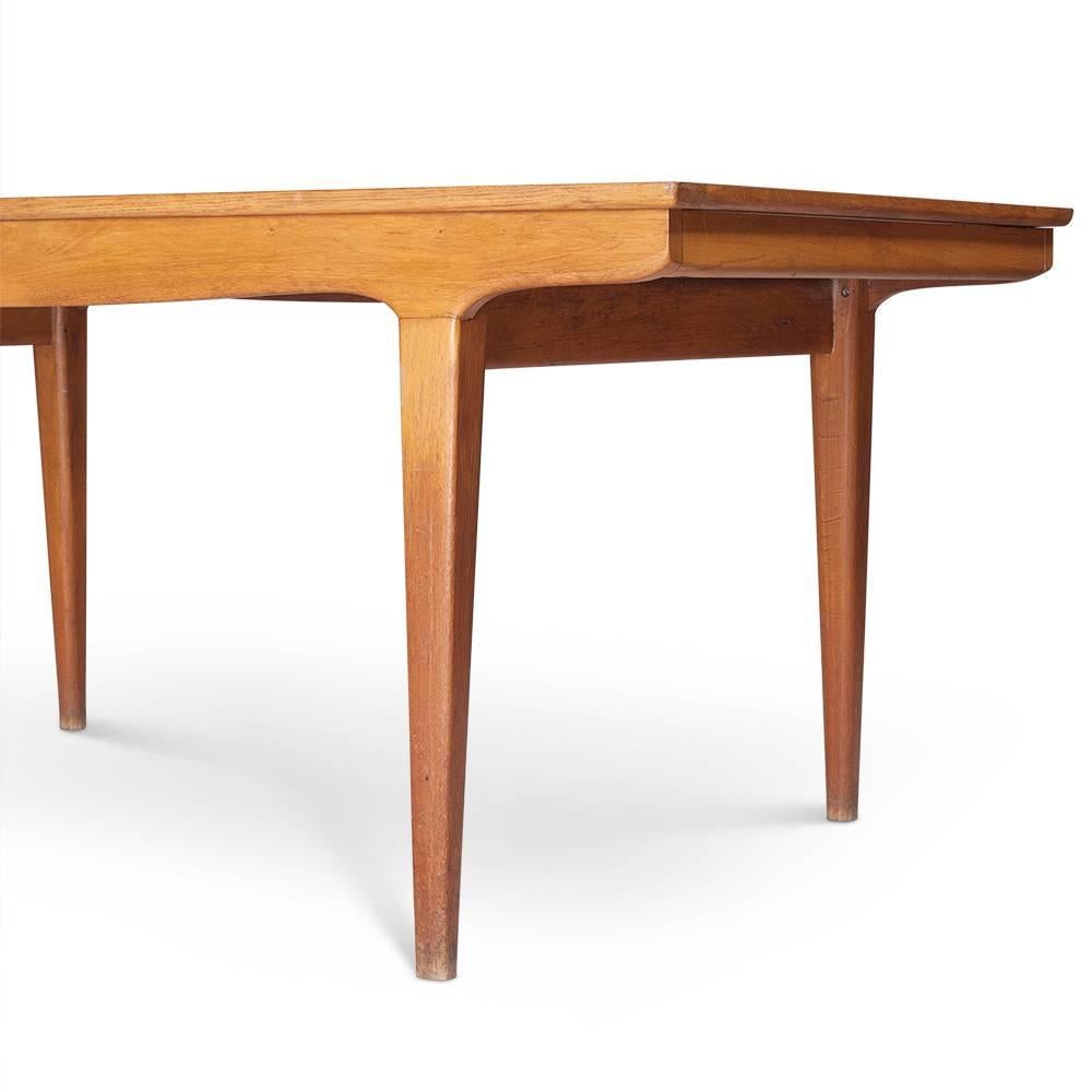 A sleek and distinctly Danish oak dining table in the style of Johannes Anderson with fluidly shaped, tapering legs. This table is extendable but the leaves are missing. Seats up to ten people when expanded. Made in Denmark.