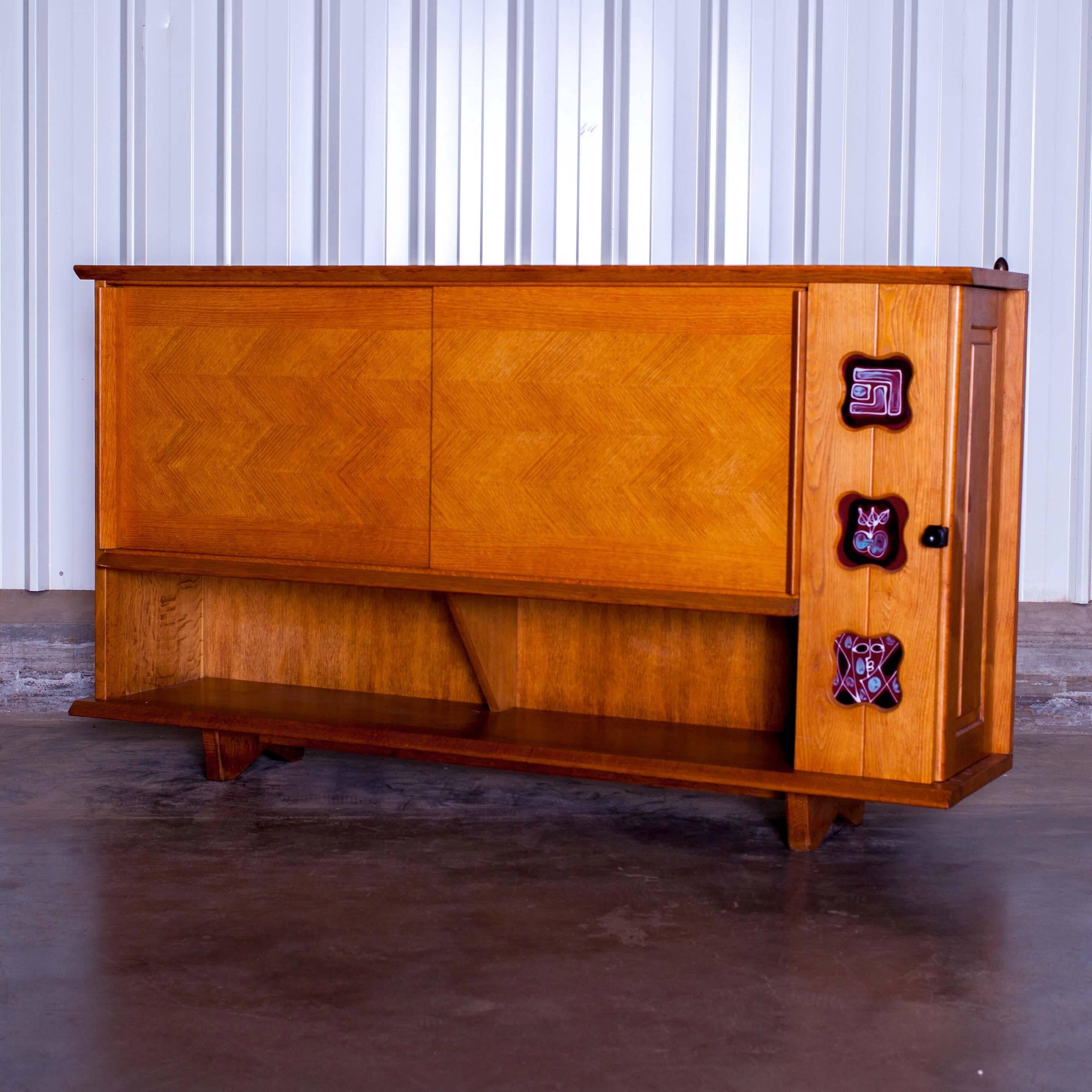 Oak sideboard
This piece was made by the French duo Guillerme and Chambron for Votre Maison in the 1960s. 
The sideboard contains two sliding doors in the front, and a door in one side hiding a bar. The top of the sideboard is decorated with six