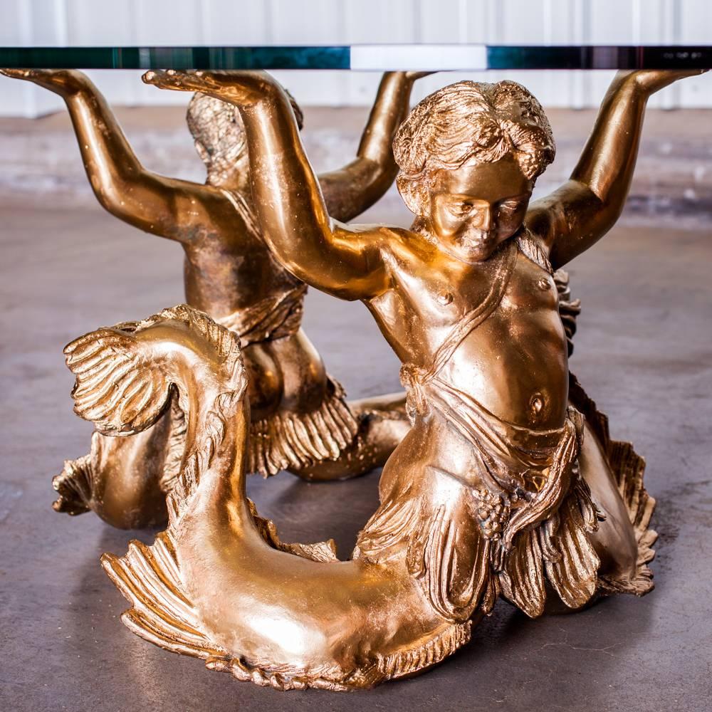 This coffee table represent two mermen connected by the tails. The bronze is gilded and the glass is oval. Very decorative.