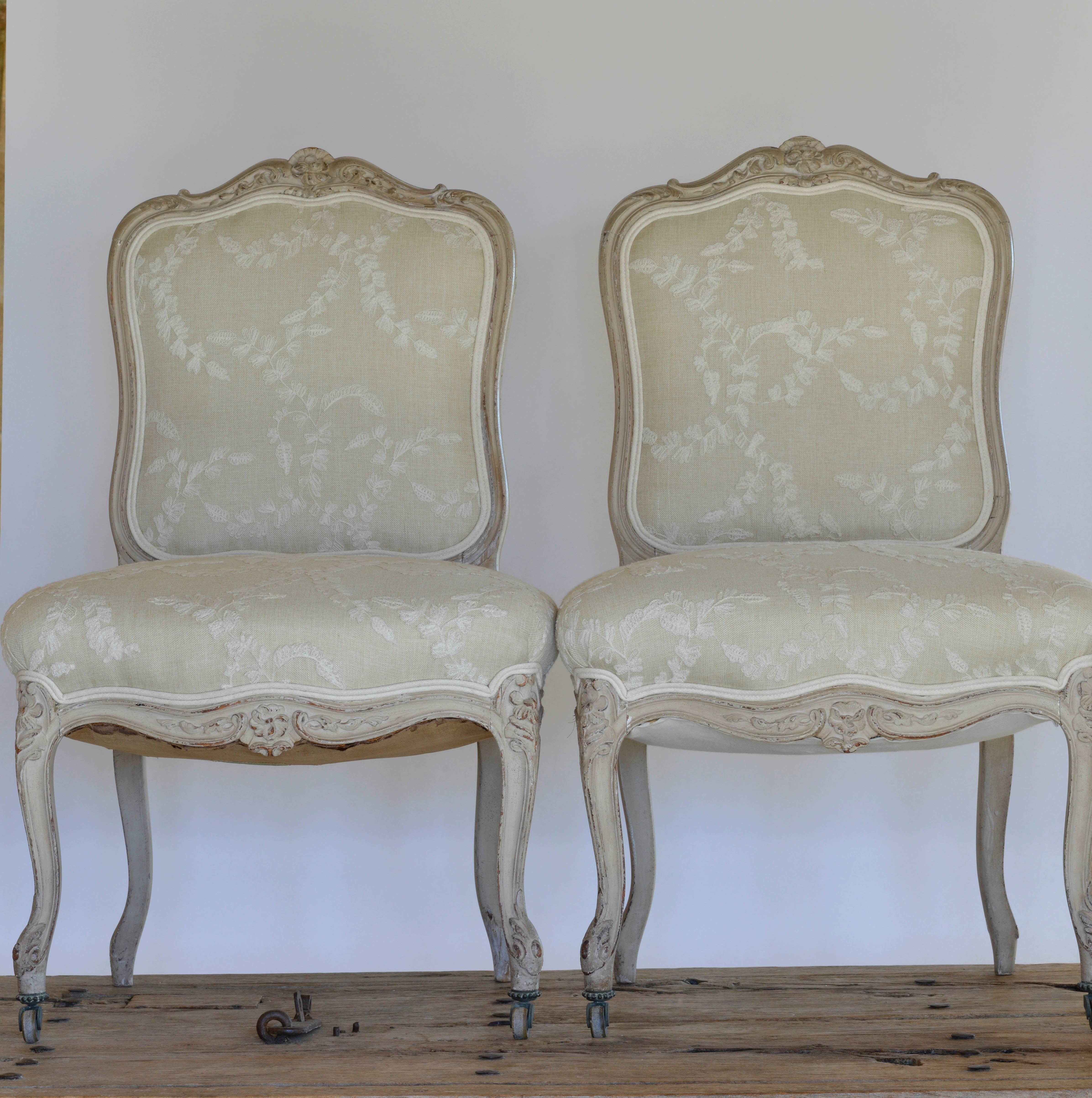This pair of French side chairs with original painted finish, original castered feet and reupholstered in a Crewel linen fit in any decor.