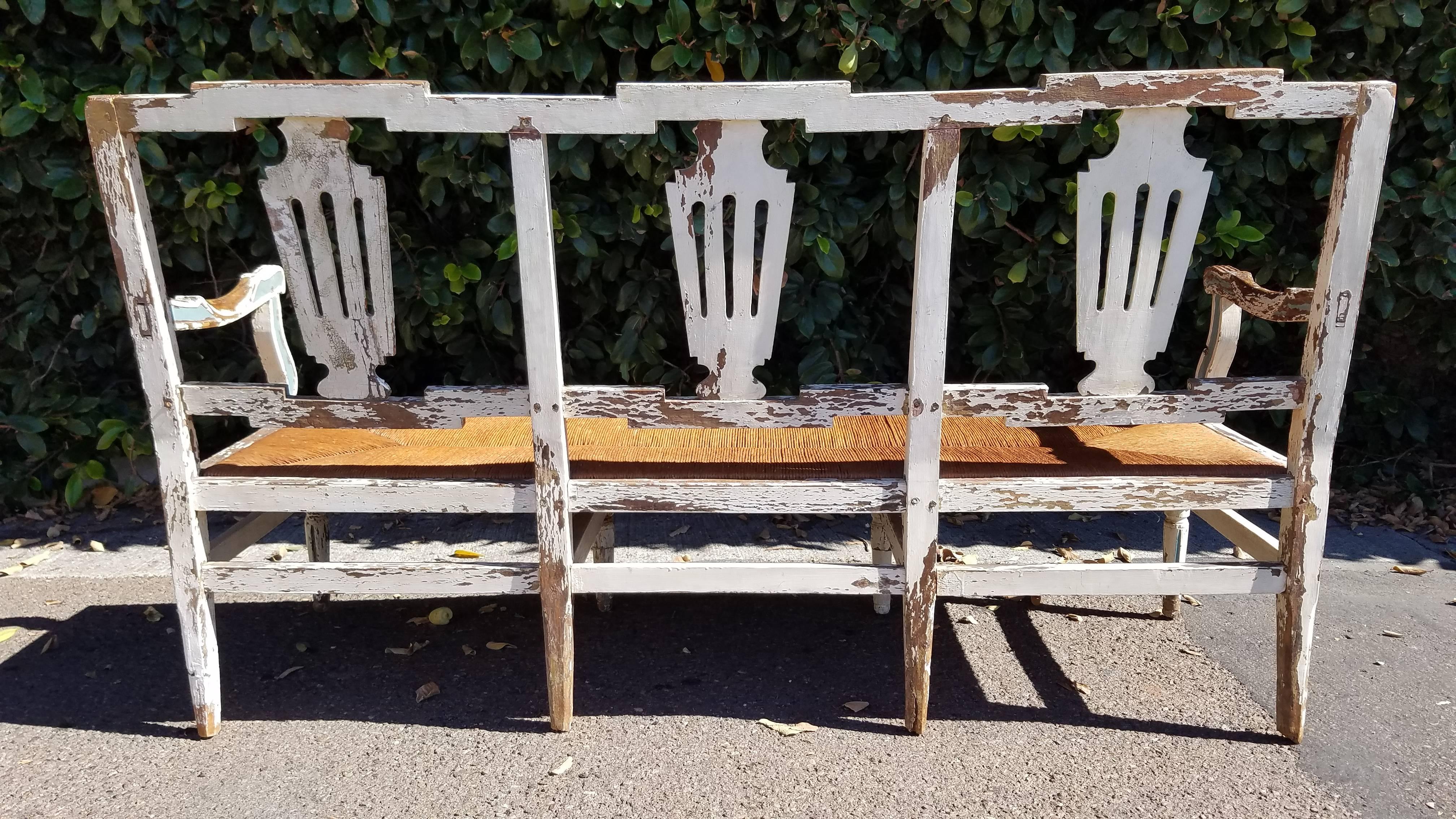 This antique settee is in very sturdy condition with a replaced rush seat and beautiful painted distress.