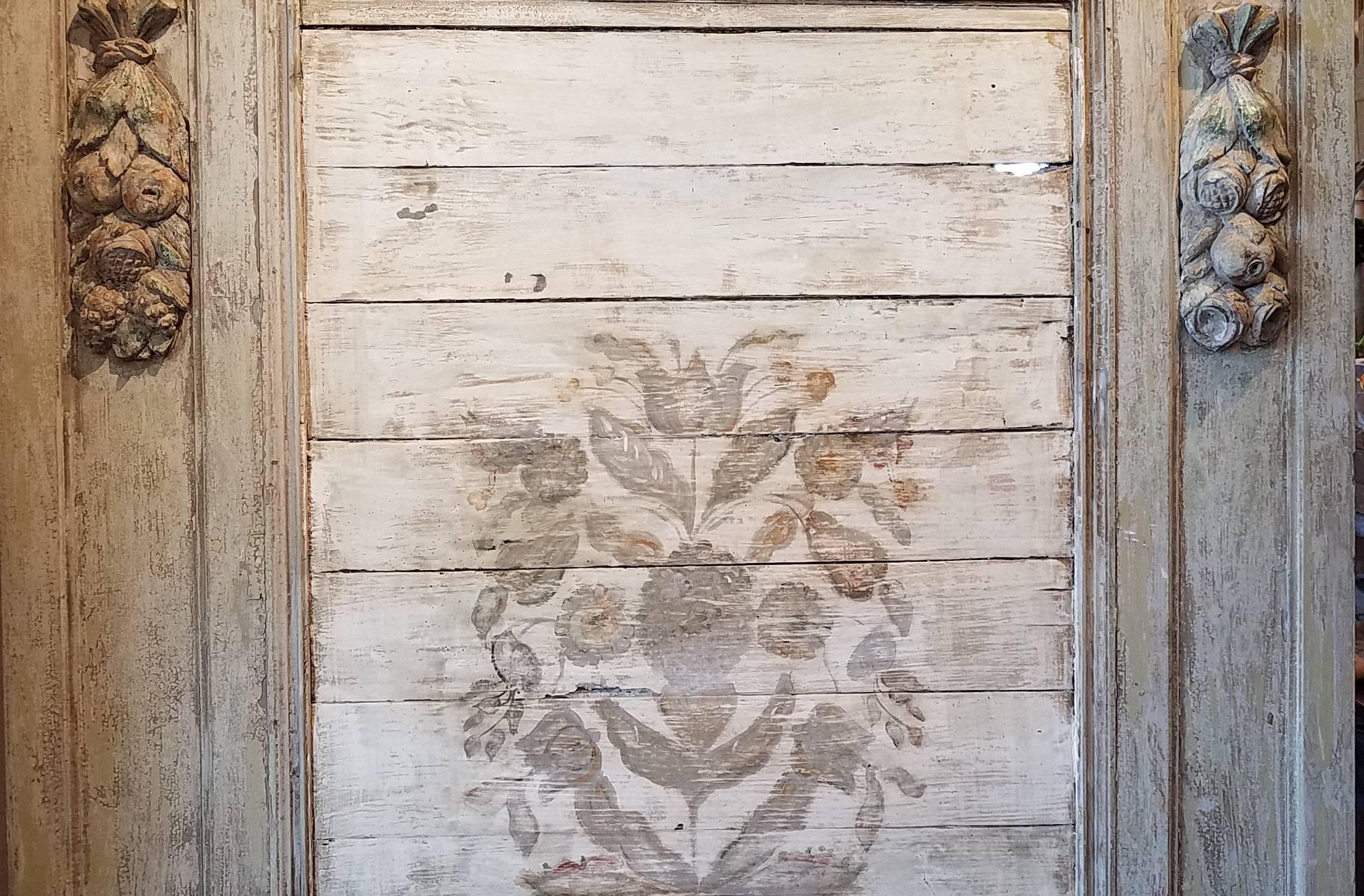 Lots of character in this mirror with the horizontal slatted front and rustic painted floral design and richly carved hanging fruit garland. Some old repair and distressed and in some places chippy paint. Mirror has been replaced.