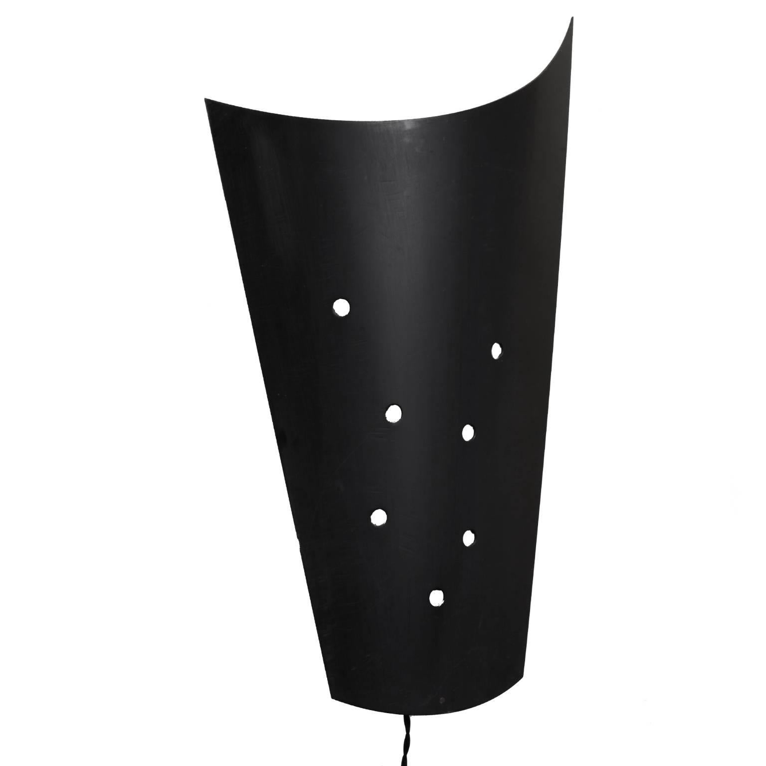 Sourced from a French cinema, this pair of black metal sconces dates to the 1980s. The postmodern design’s perforated holes create a constellation of light. A curved, conical shape directs up-and down-lights while concealing a double socket and