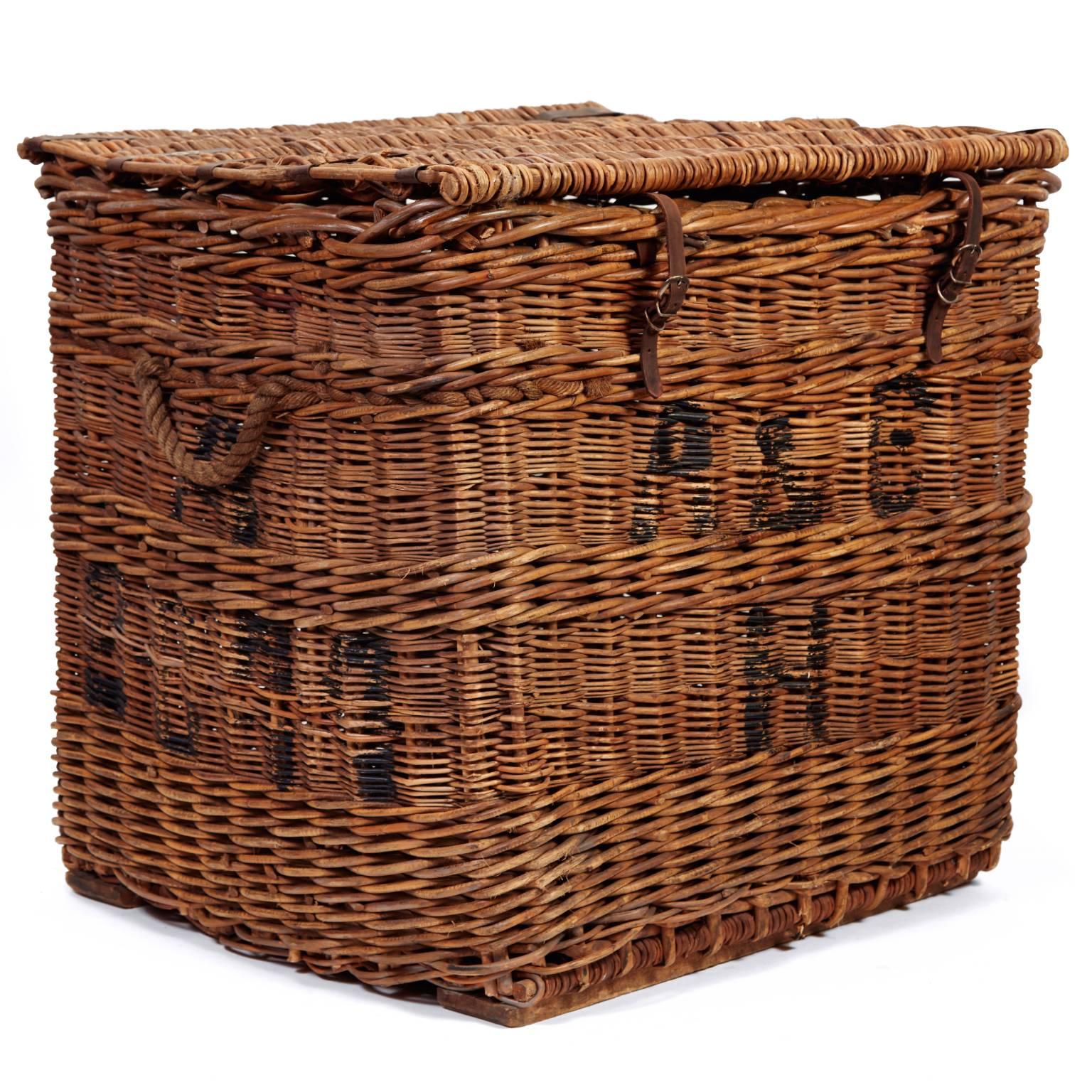 Once used for sorting and shipping letters, this vintage French mail basket is woven from rattan on a sturdy square frame. The lid closes with leather hinges, straps and metal buckles. The sides feature stenciled letters, and rope handles make it