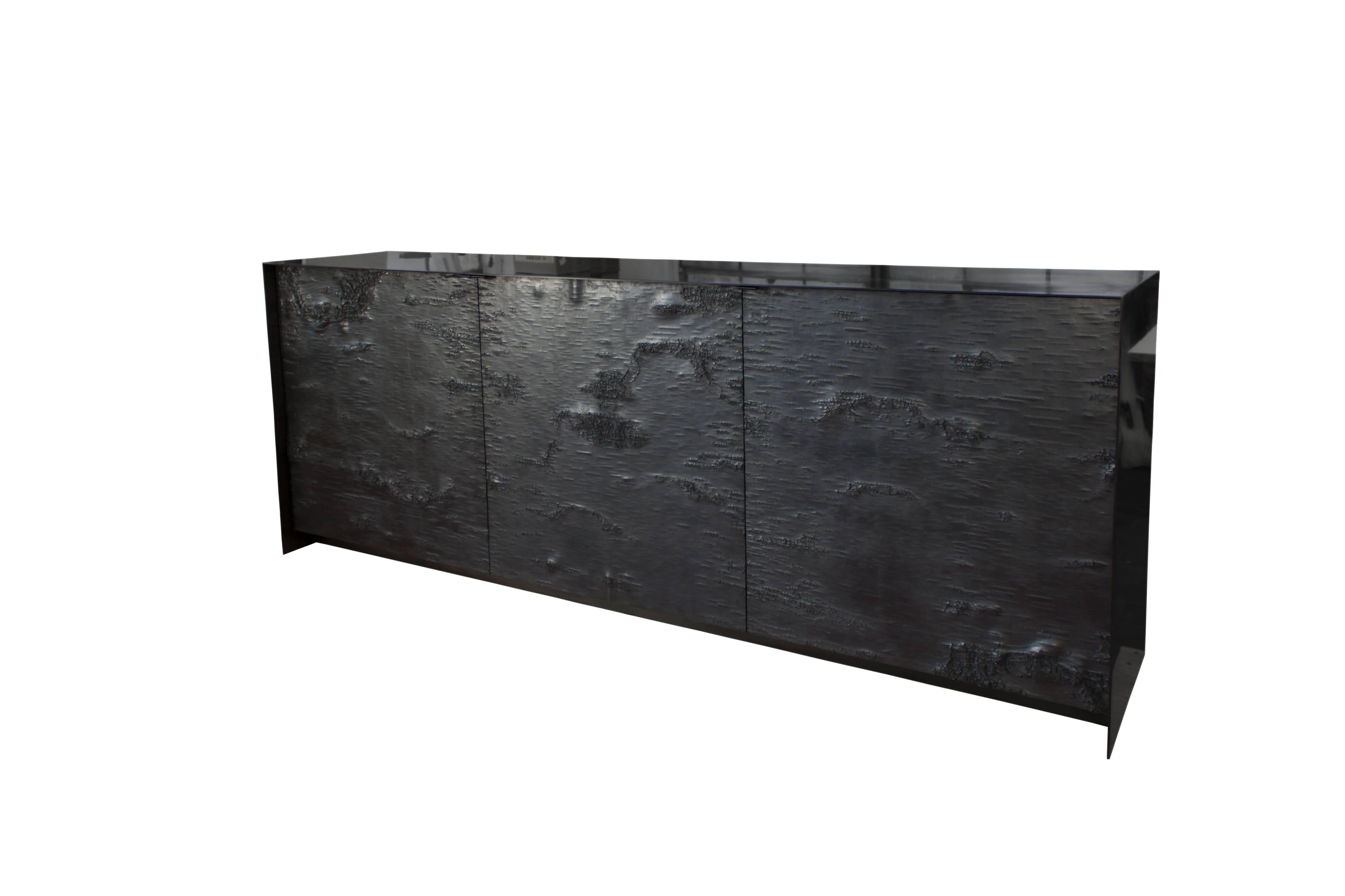 High detail textured birch bark doors executed in Ether Atelier’s exclusive Graphite cast finish deliver the perfect counterpoint to the sharp lines of the luster gunmetal black steel surround in unlacquered oil and wax finish. Ebonized Ash lines