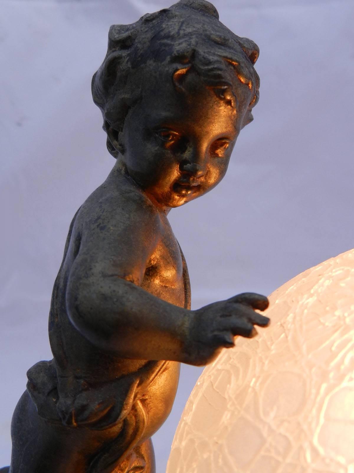 Charming French Art Deco table lamp Putti globe night light, circa 1930
Marble base, gilded spelter figure and original craquelure glass globe
In very good condition with no losses to glass, gilding has a good patina worn through time and use
This