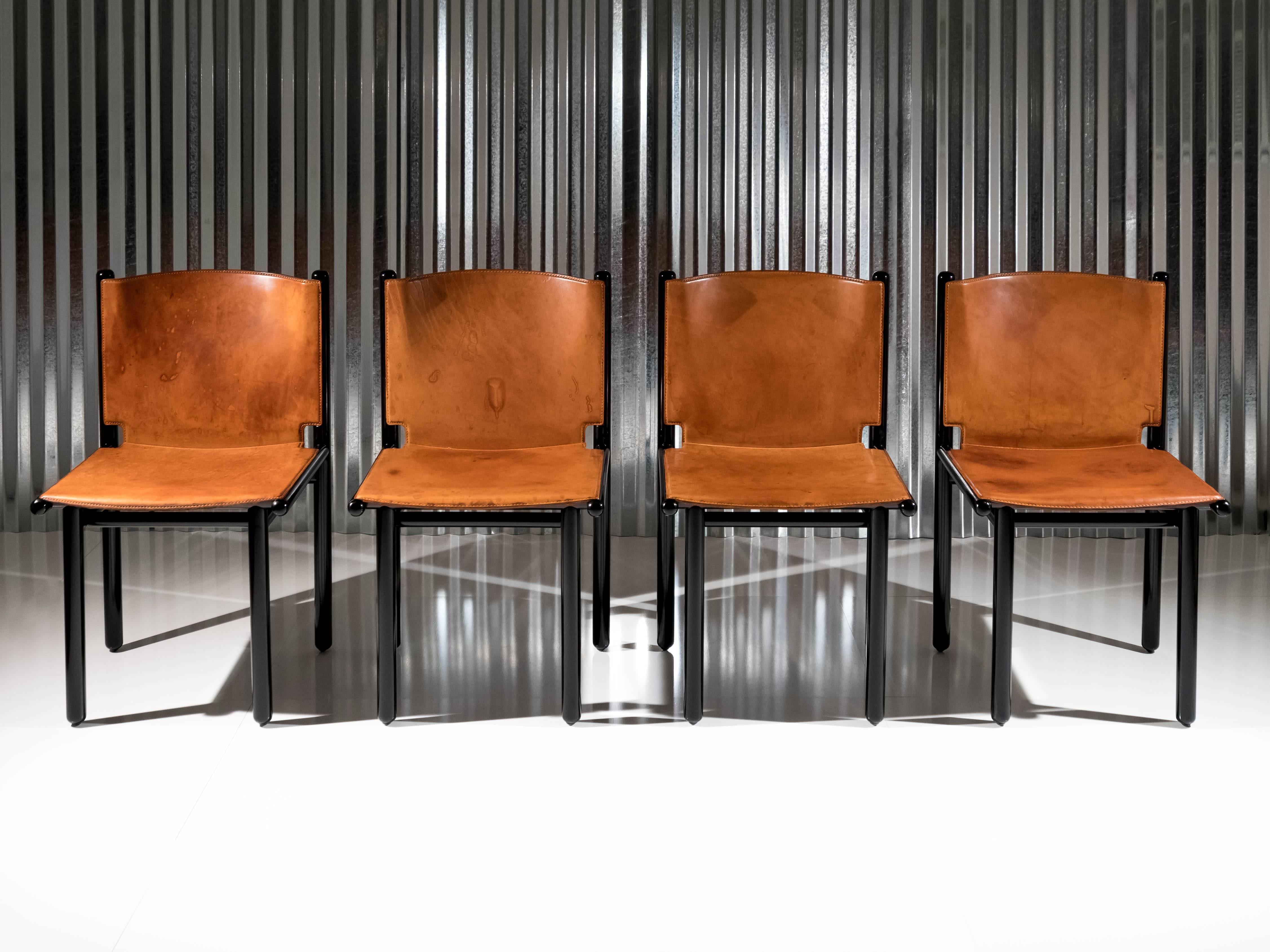 This set of four 'Caprile' chairs designed by Gianfranco Frattini for Cassina in 1985 display an elegant black lacquer finish that contrasts with the natural saddle leather molded seat and back. Designed by Frattini after spending the previous year
