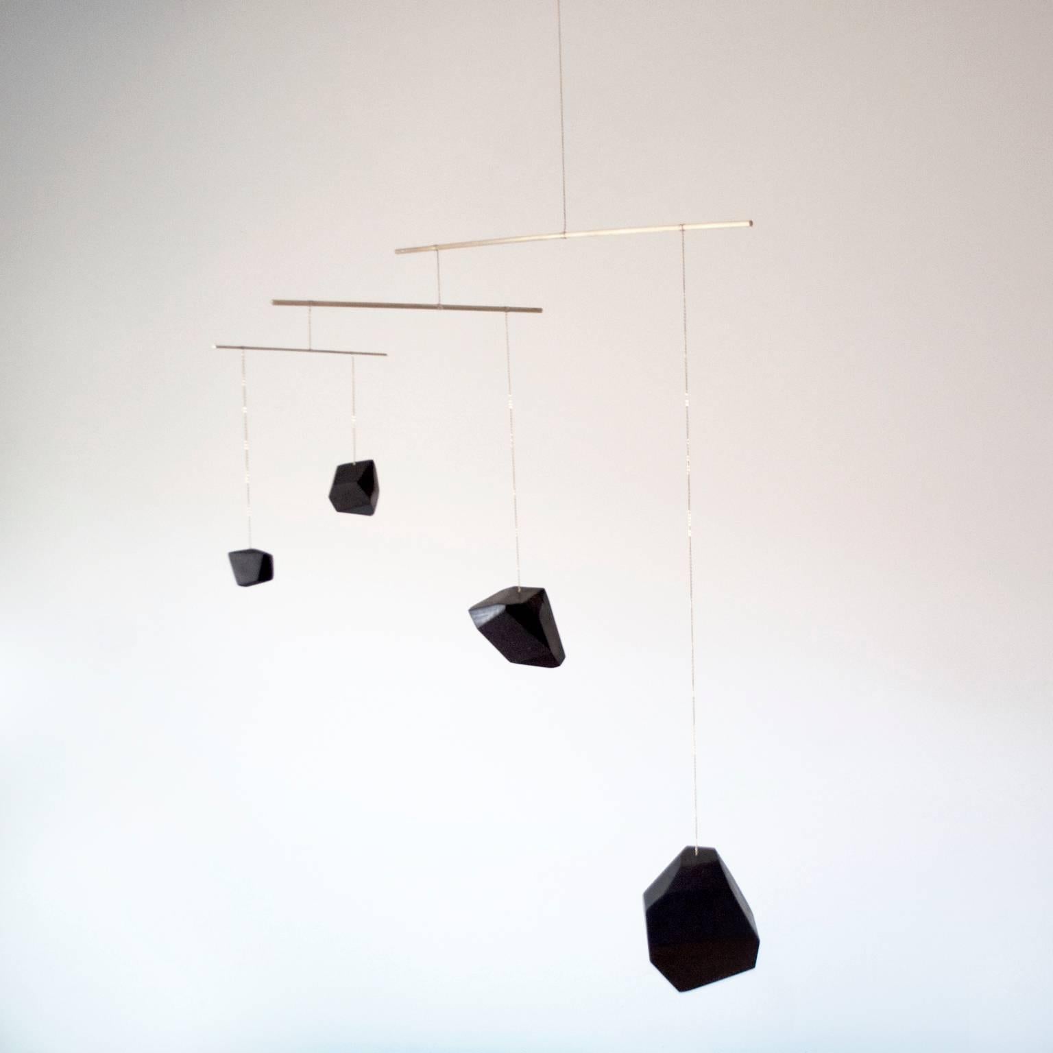 Large mobiles are made from solid walnut blocks which are hand-sculpted and slowly polished using vegetable soot ink until a hardened black surface approaches chatoyancy over the wood’s grain. Four or more blocks are then arranged, silver soldered