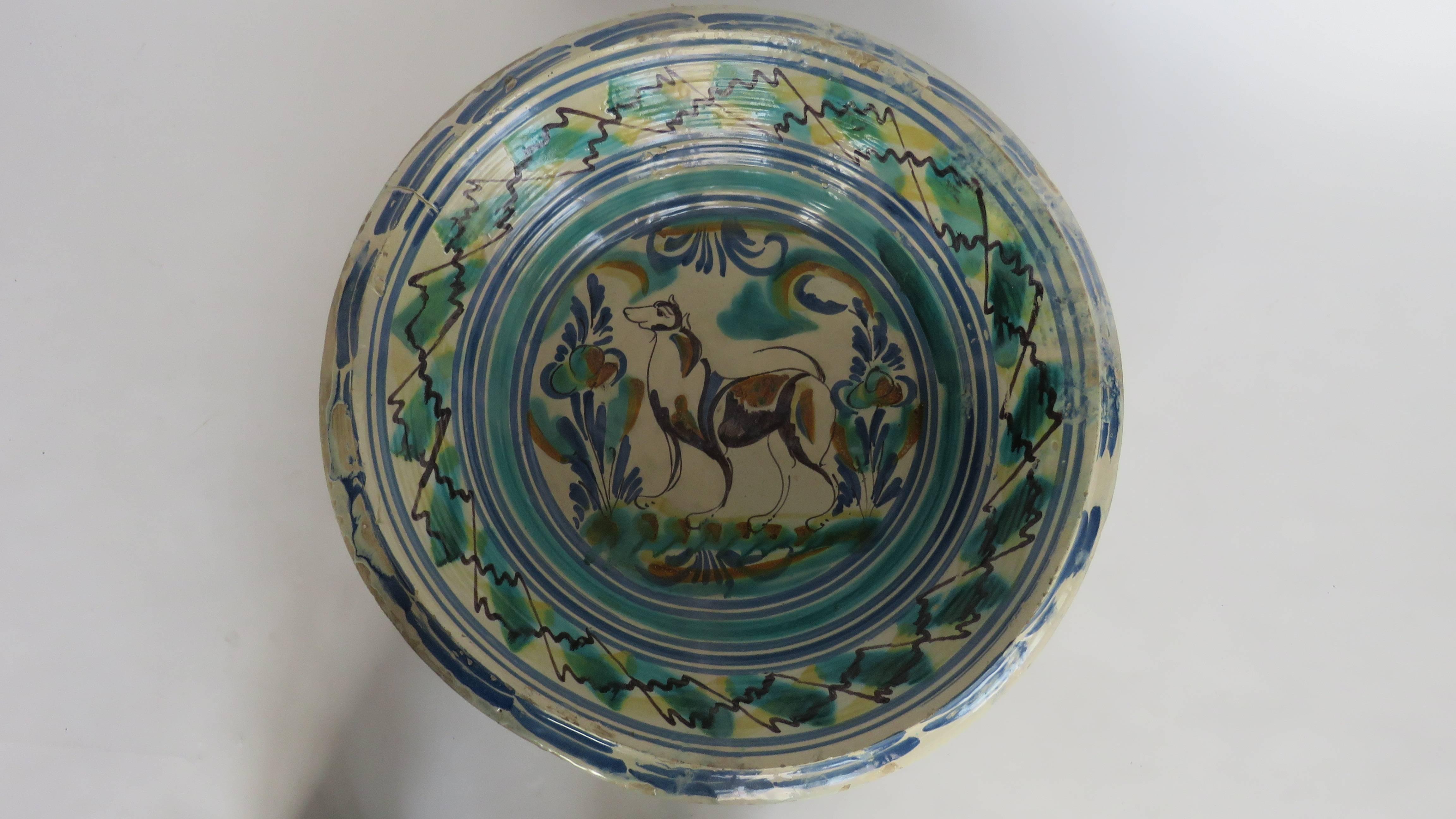 Glazes of copper green, cobalt blue, yellow and manganese on a bone white slip depicting a dog in a landscape setting with flowers. Origin: Sevilla, Spain.

Iron support not included.