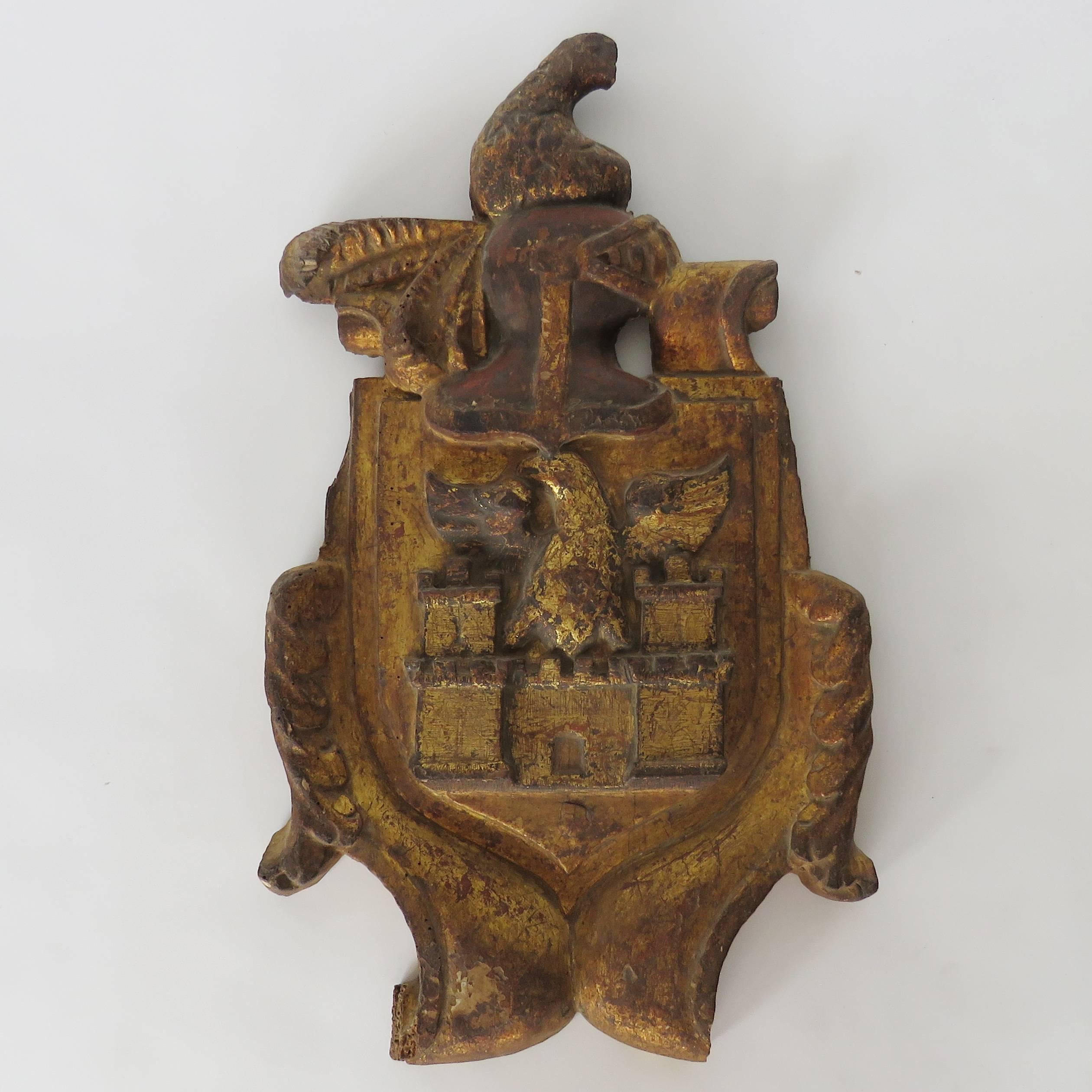 Chunky carved giltwood coat of arms. The depictions represent an eagle over a castle. The helmet represents significant bravery in a battle for which the family received a Royal honour probably a Lordship or Knighthood.