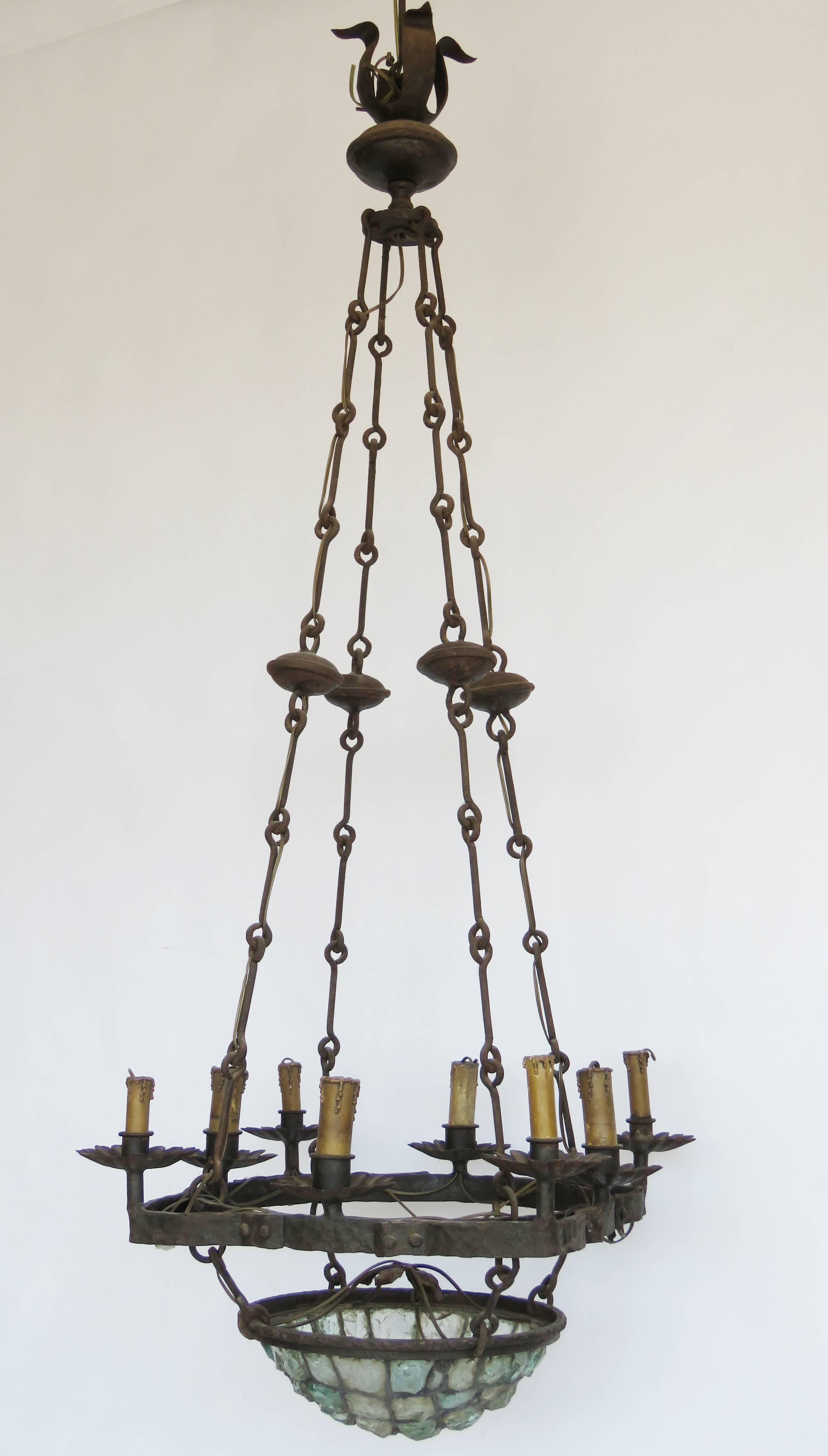 Large hand-forged iron chandelier suspended on rod and ring irons, eight candle lights on an unusual shape base a further light in the rock crystal hanging basket.

Antoni Gaudi style design.