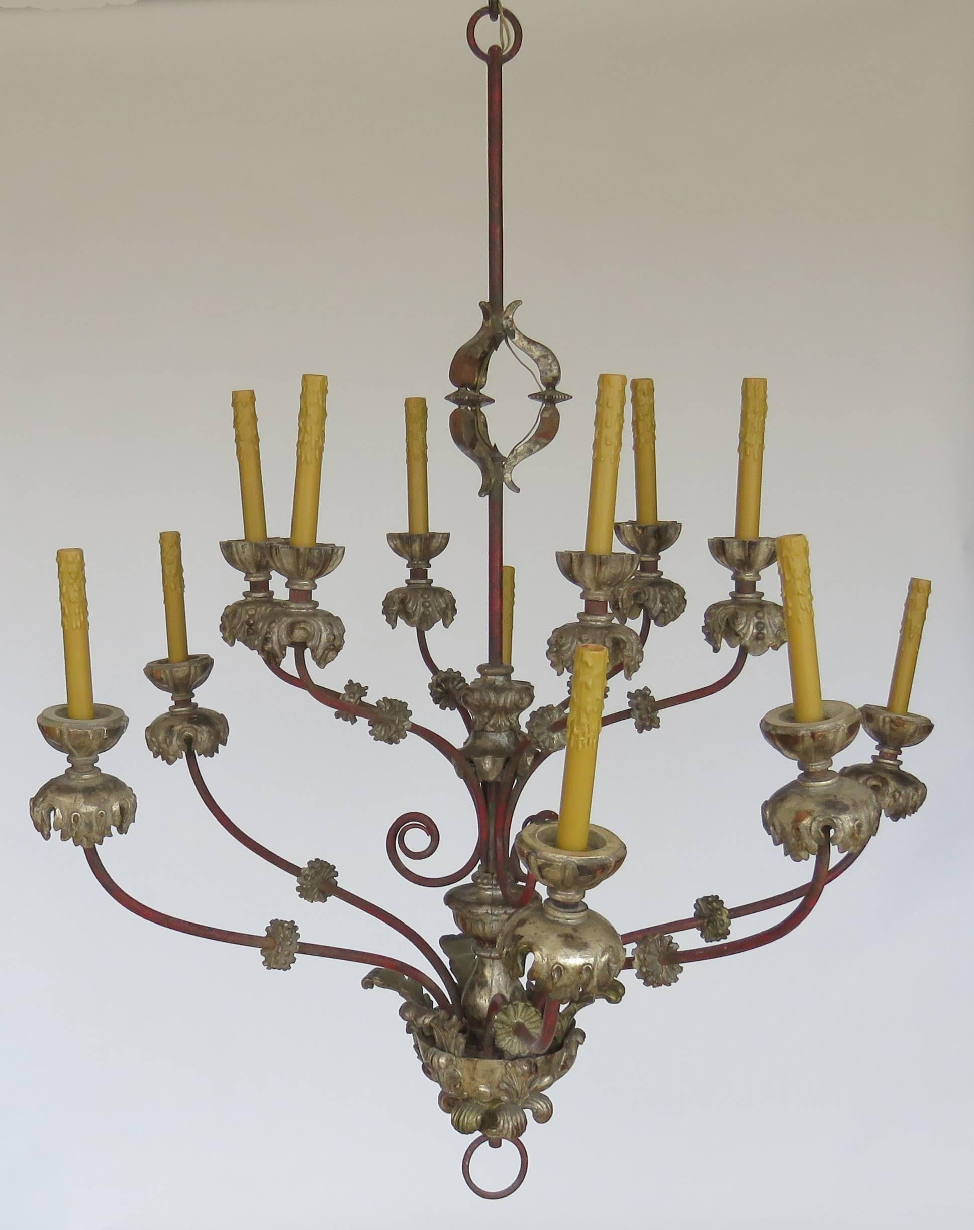 Unusual hollow iron chandelier with decorative wooden bobèches, having a distressed painted finish, with two tiers of six scroll candle arms. Original paint.

The chandelier is shipped disassembled.