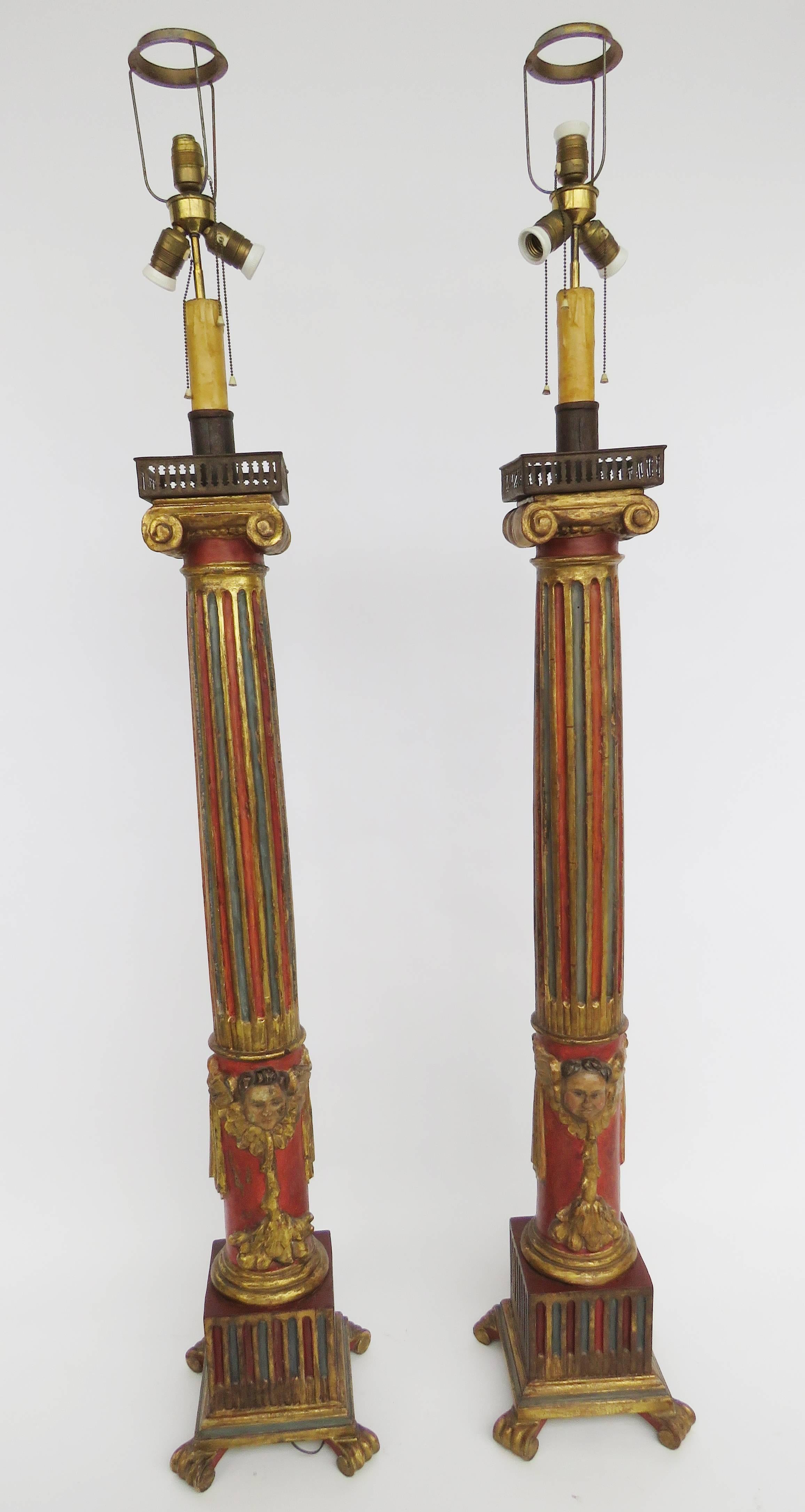 Red, blue and gold highly decorated fluted column surmounted by square scrolled platforms with iron candle holders, lower column with mask and swag carving, raised on square plinth and paw feet.