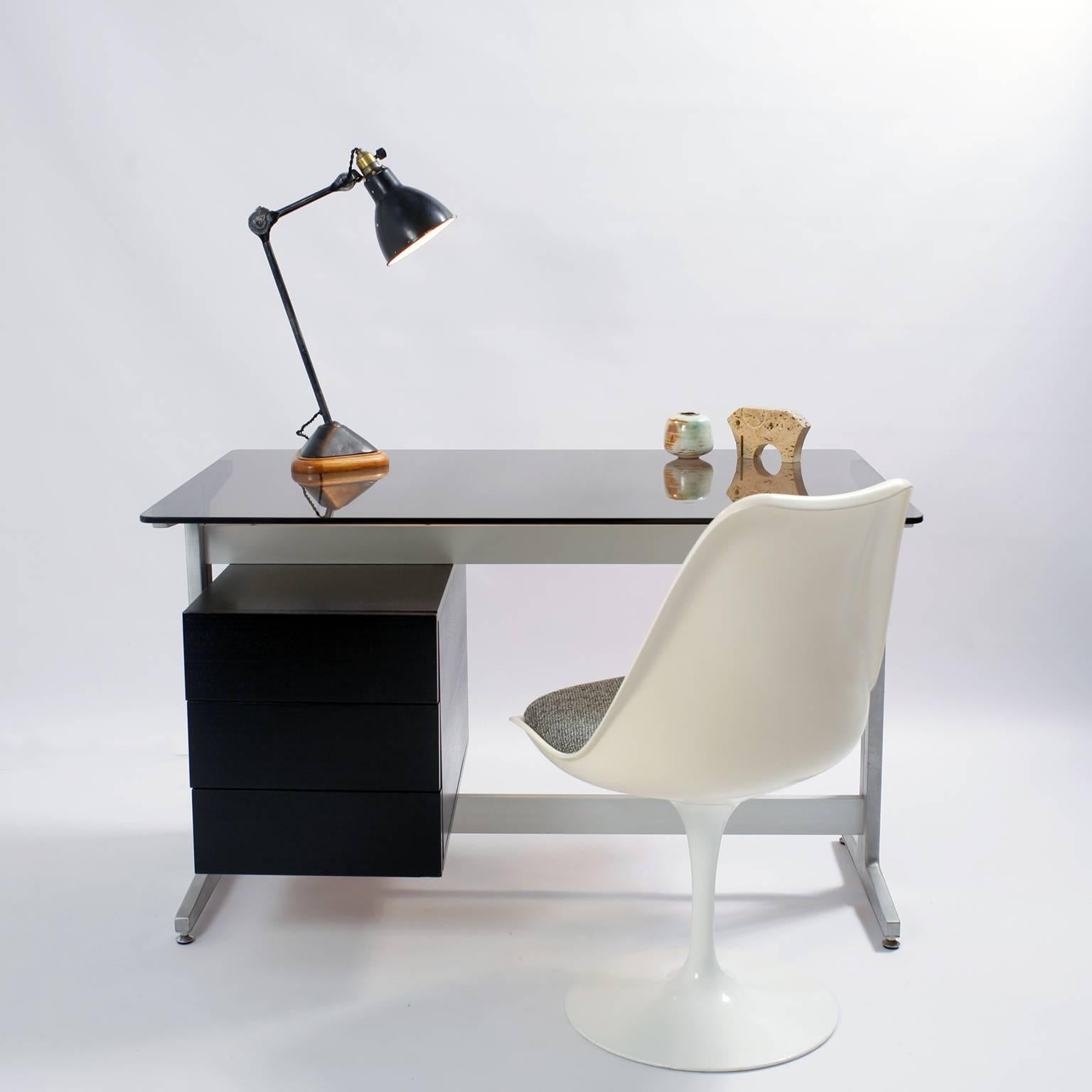 Desk by French designer Etienne Fermigier dating from the 1970s. It has a smoked glass top one hanging cabinet opening by three drawers in blackened wooden, and rests on a brushed aluminium base.