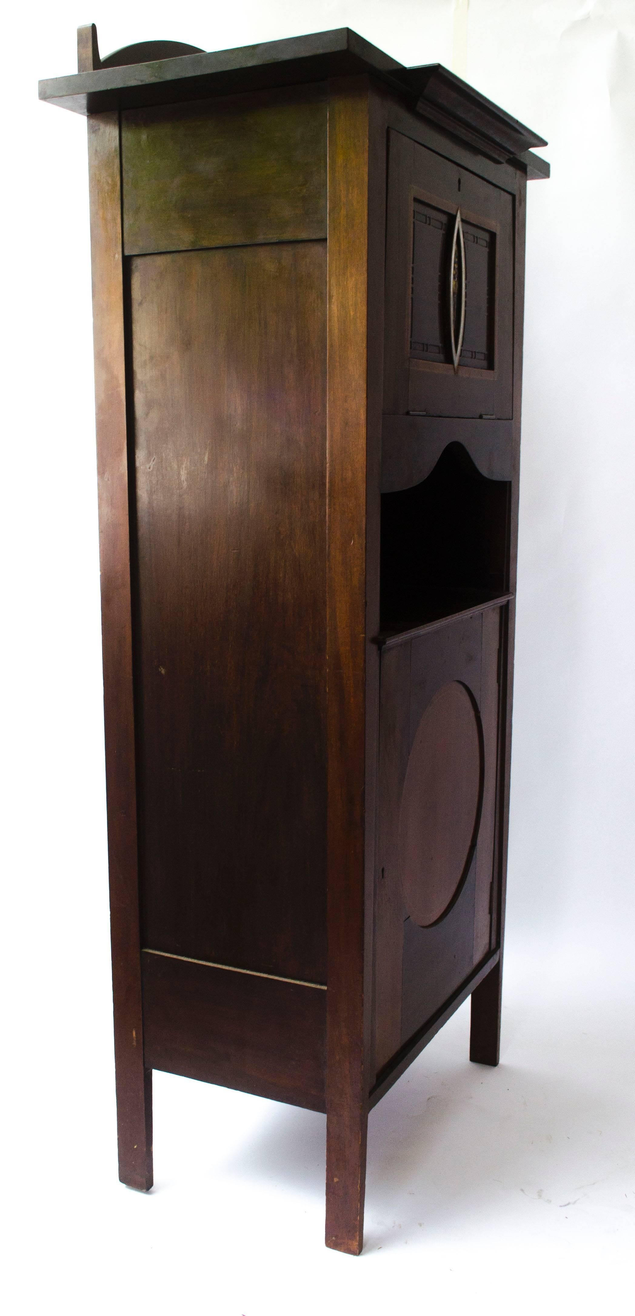 Arts and Crafts Mahogany Music Cabinet designed by G M Ellwood made by J S Henry with a Scottish style enamel plaque to the centre of the upper door, the plaque attributed to Jessie M King, surrounded by pewter inlay and pewter squares.