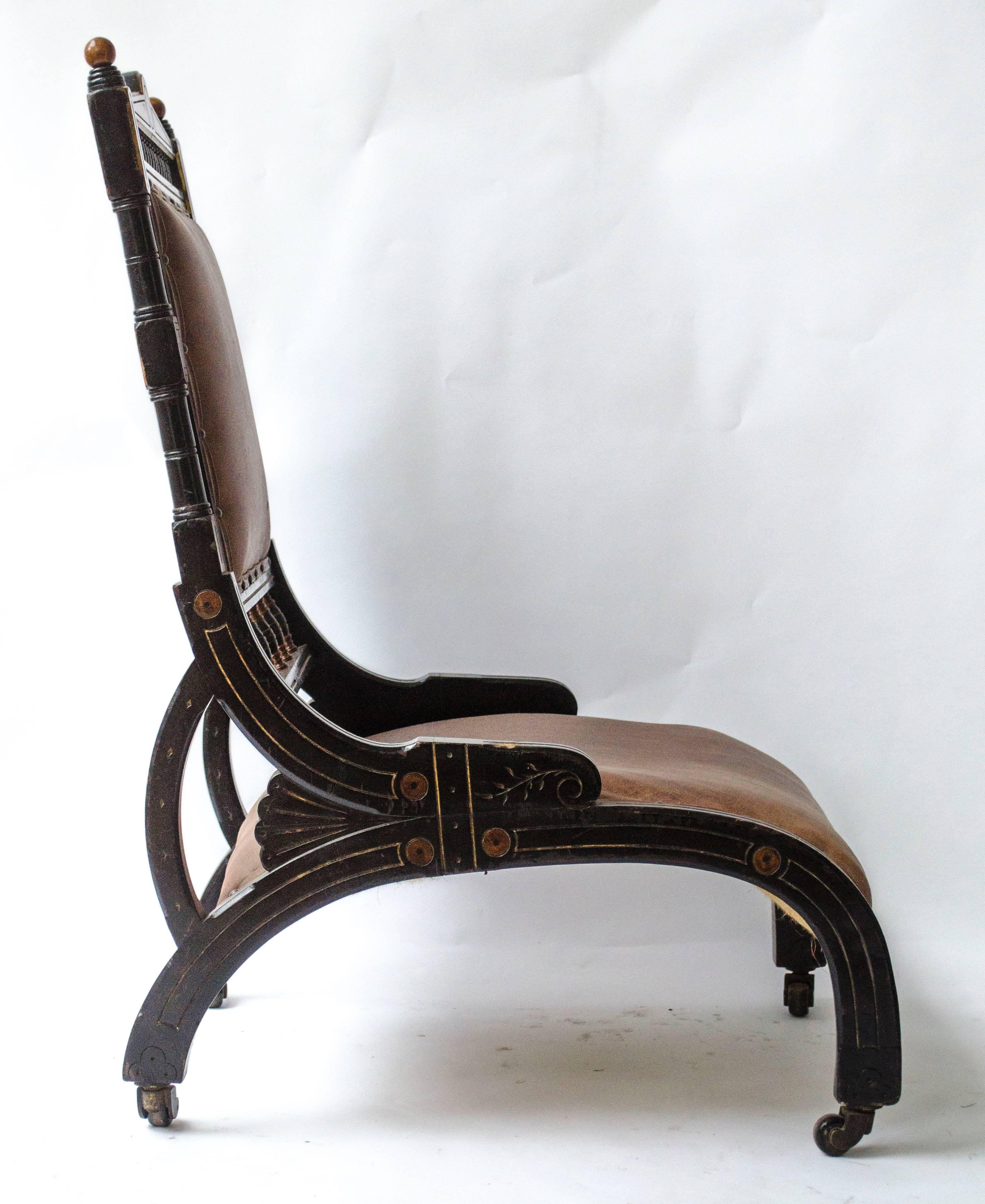 Richard Charles (1823-93), A rare Aesthetic Movement ebonized and parcel Gilt lounge chair, with a spindle gallery above and below the padded back rest, with arched shaped legs to each side from front to back also forming the seat and a smaller
