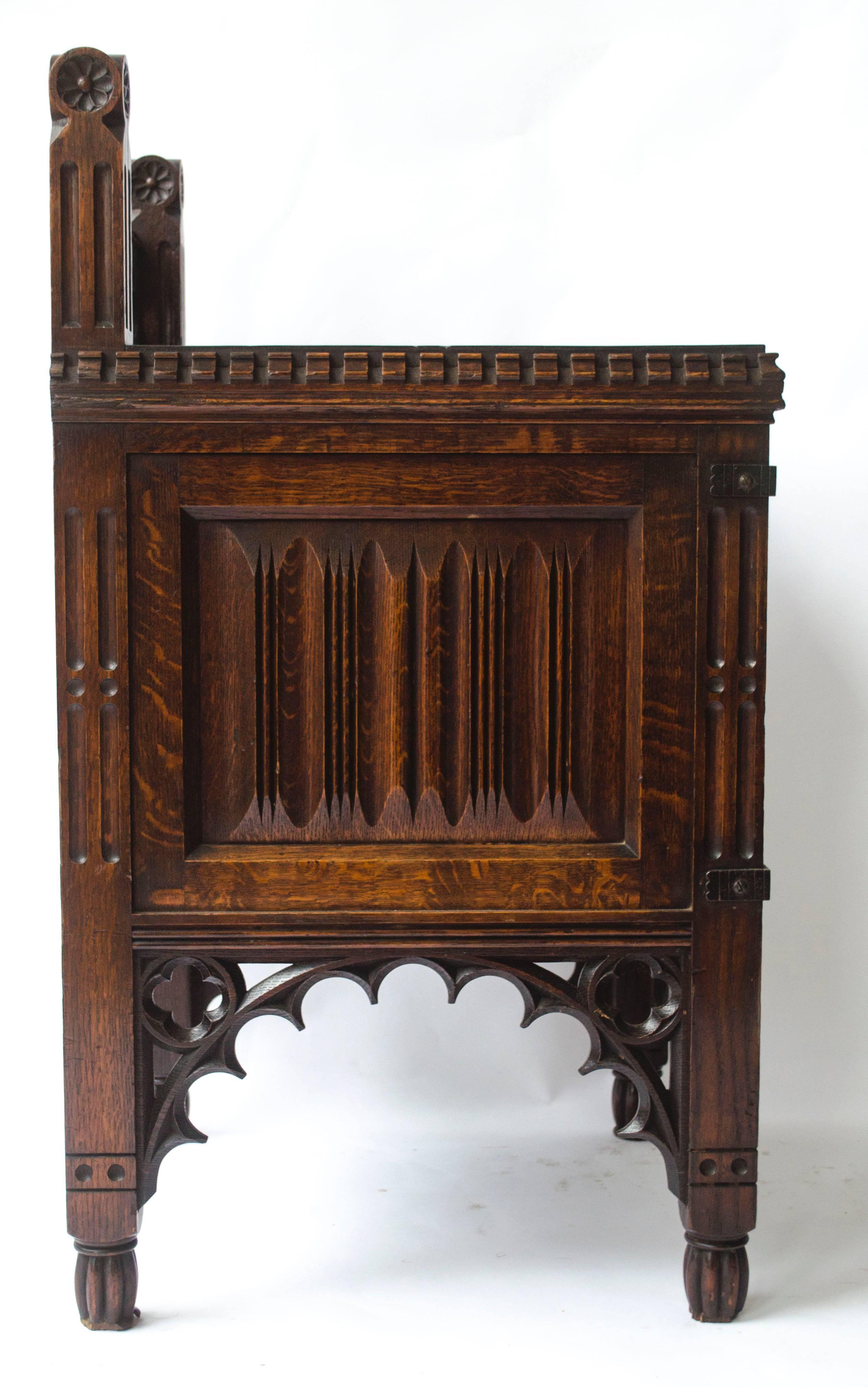 Bruce Talbert attributed Gothic Revival Oak Night Table with carved quatrefoil details to the top, carved uprights and dentil carved details around the work area, the door and sides with carved linen fold details with stylised brass strap hinges and