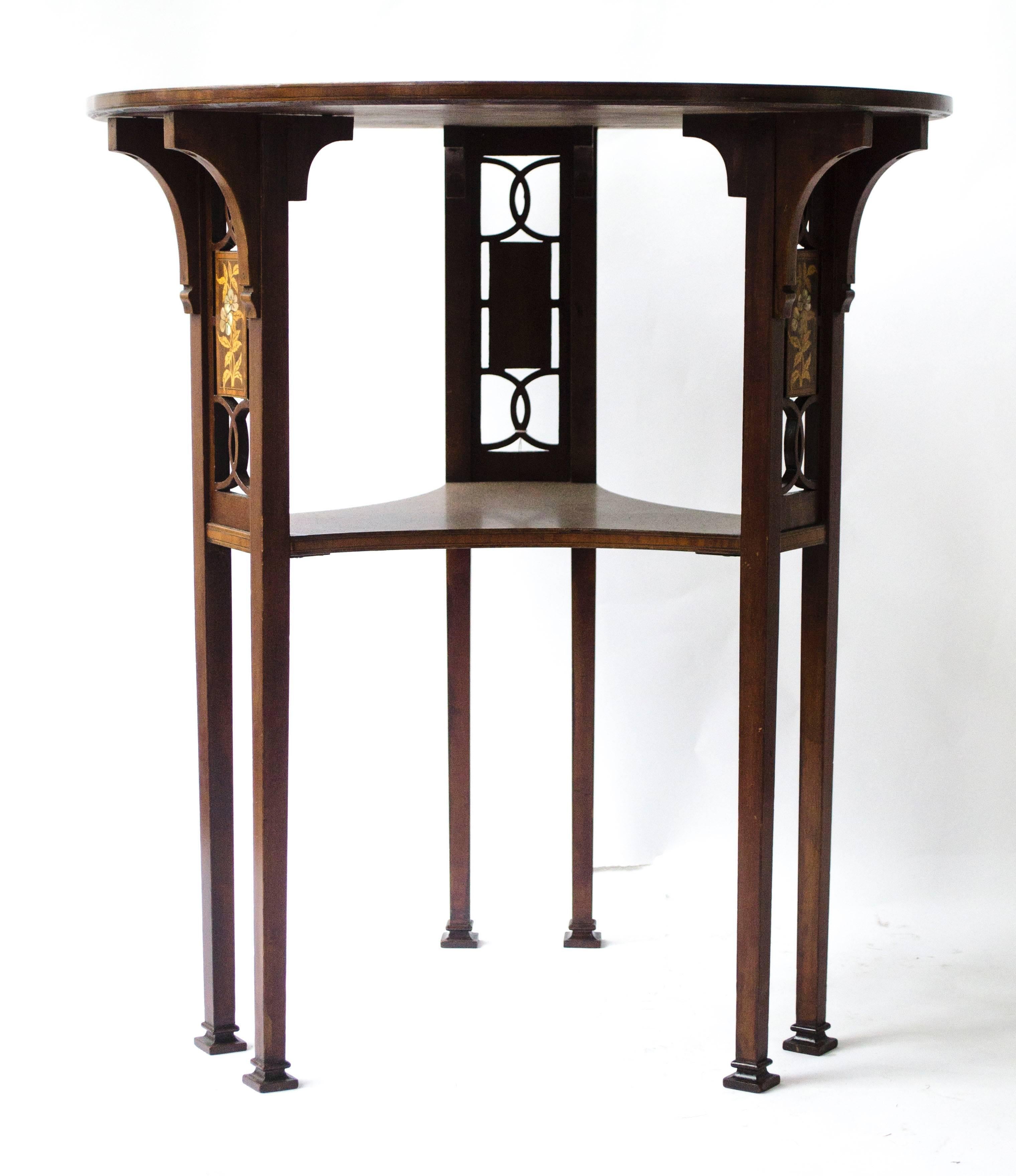 A Liberty and Co Arts & Crafts circular mahogany side table with six legs, united by a central shaped shelf, the sides with floral inlays with mother of pearl and fruit woods.