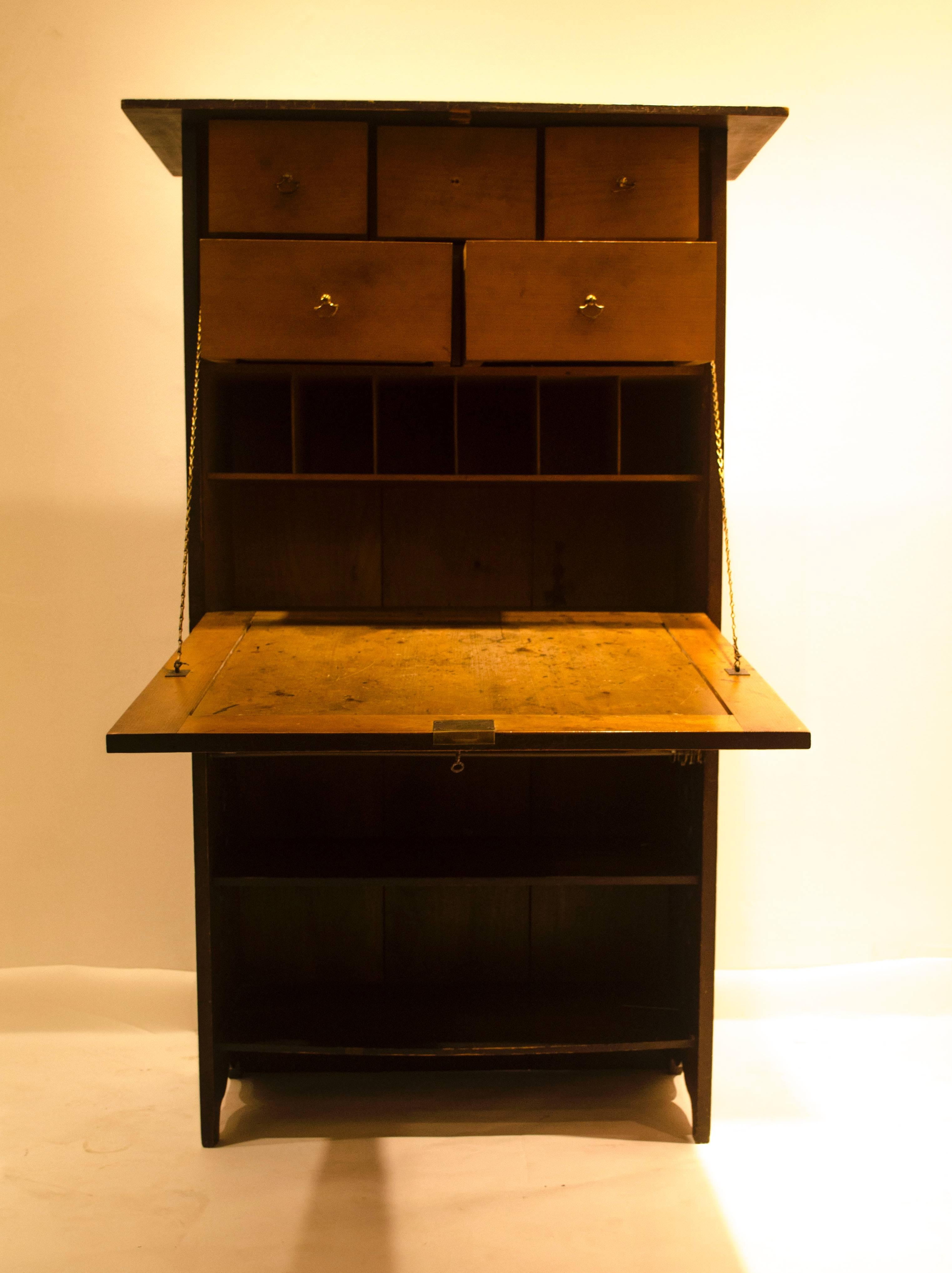 Charles Rennie Mackintosh (1868-1928), a cypress wood and brass writing cabinet, formerly green stained, with large stylized fret work foliate hinges, heart escutcheons and conforming handles to the central drawer. A fold down writing area with