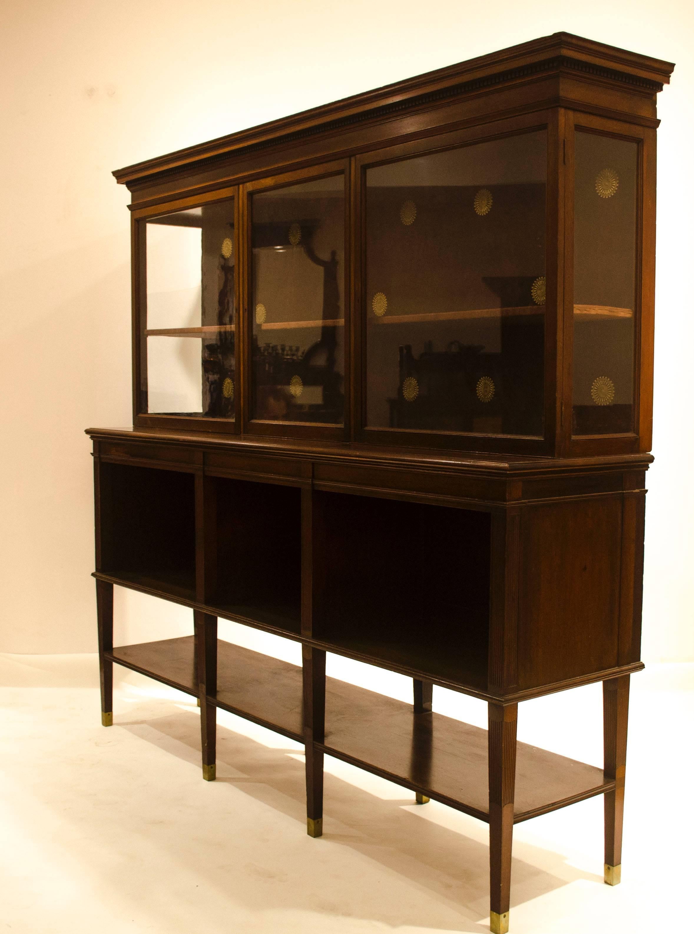 Edward William Godwin (1883-1886) for Collinson and Lock.
An Anglo-Japanese eight leg Walnut side cabinet, with dentil moulded cornice above a glazed three door cabinet, the base breaking forward with open cupboards and open shelves below, stood on
