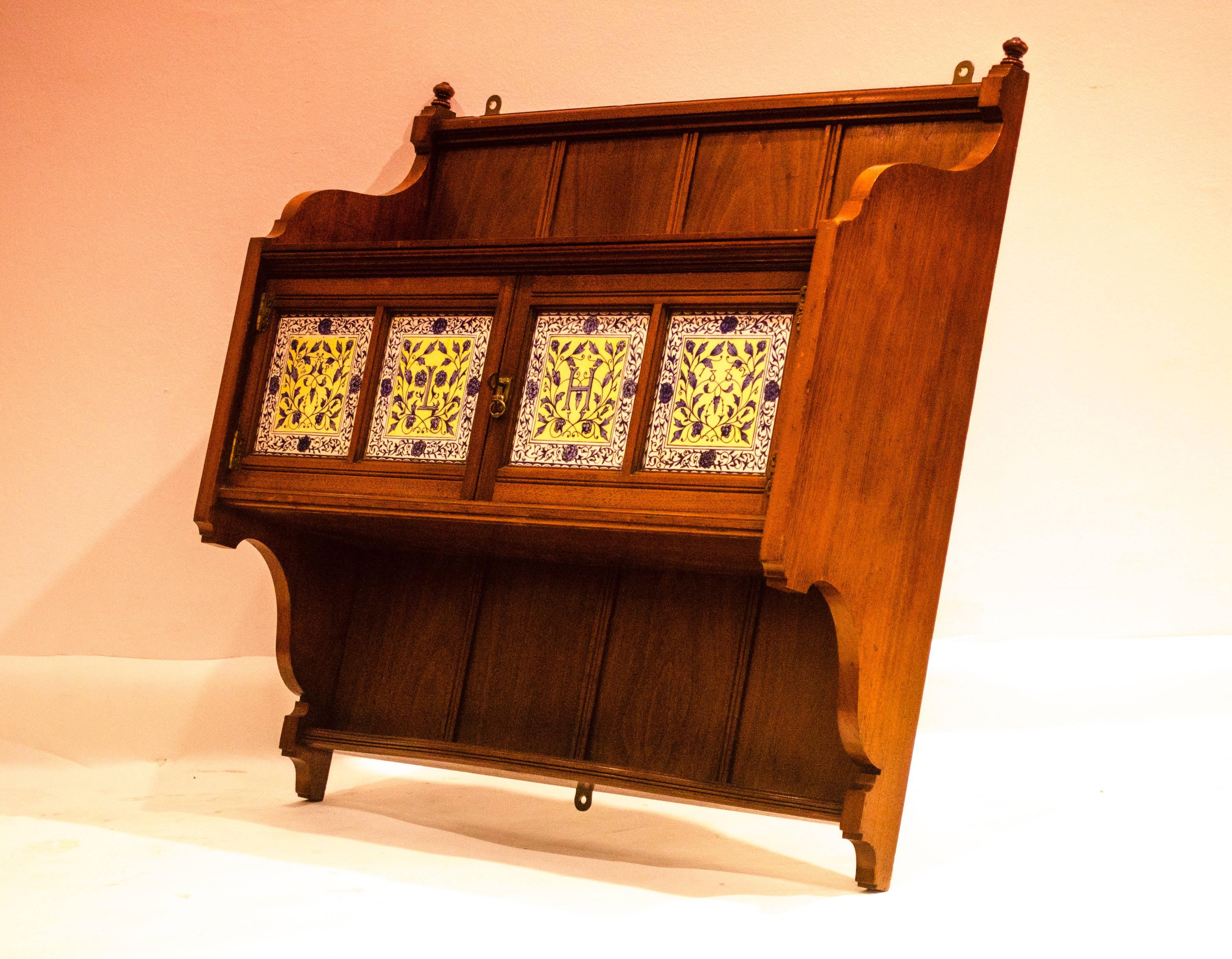 Lewis Foreman Day (attributed), a walnut and tiled wall cabinet, the tiles painted with flowers, 'L', 'H', '27th April' and '1882'. 'L', 'H' could easily be swapped to 'H', 'L'.